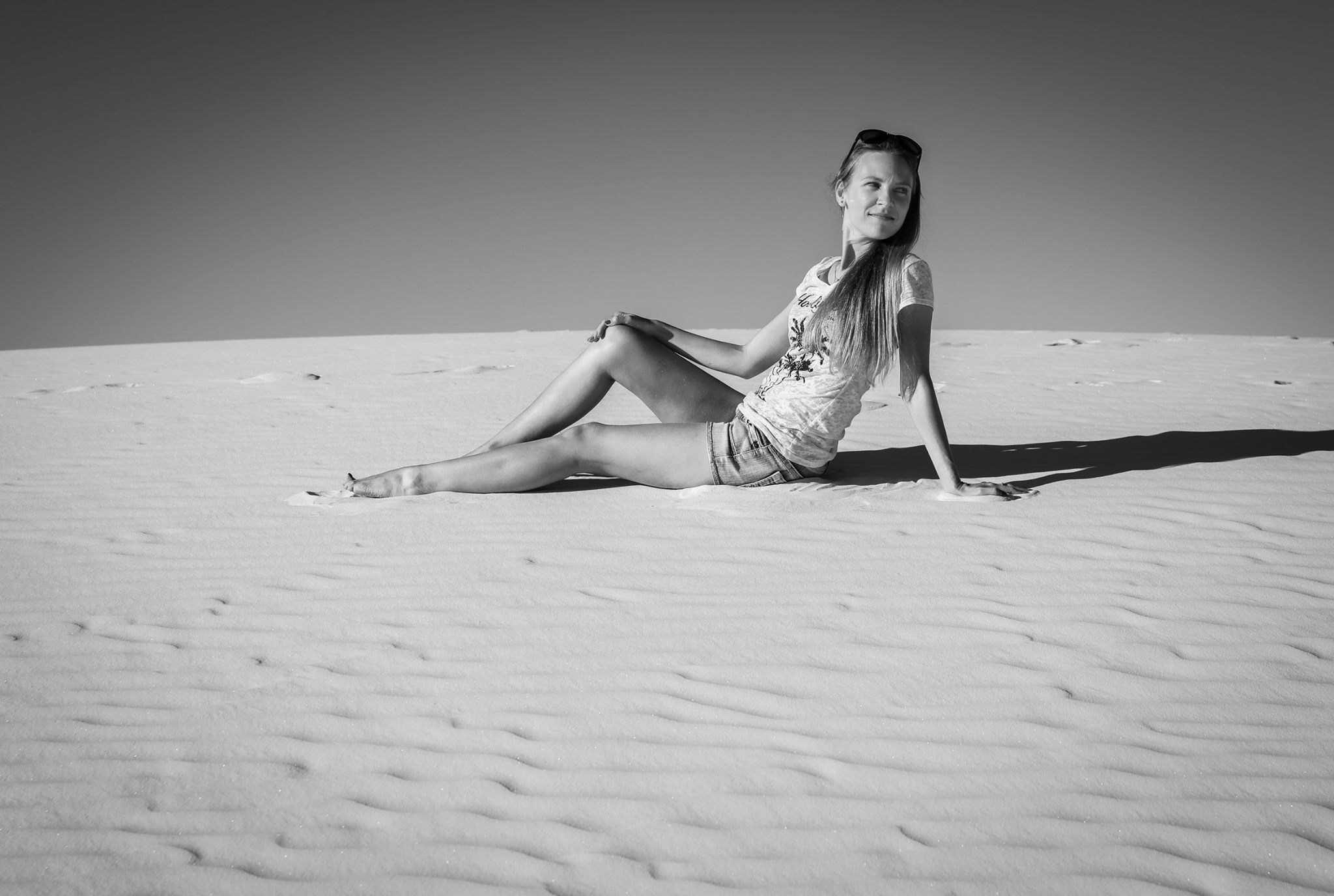 Black and white photo of a person sitting on sand dunes in a patterned dress during a sunny day.  White Sands, NM.