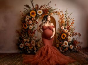 A terracotta gown flows dramatically beside autumn floral arrangements with sunflowers and dried foliage.