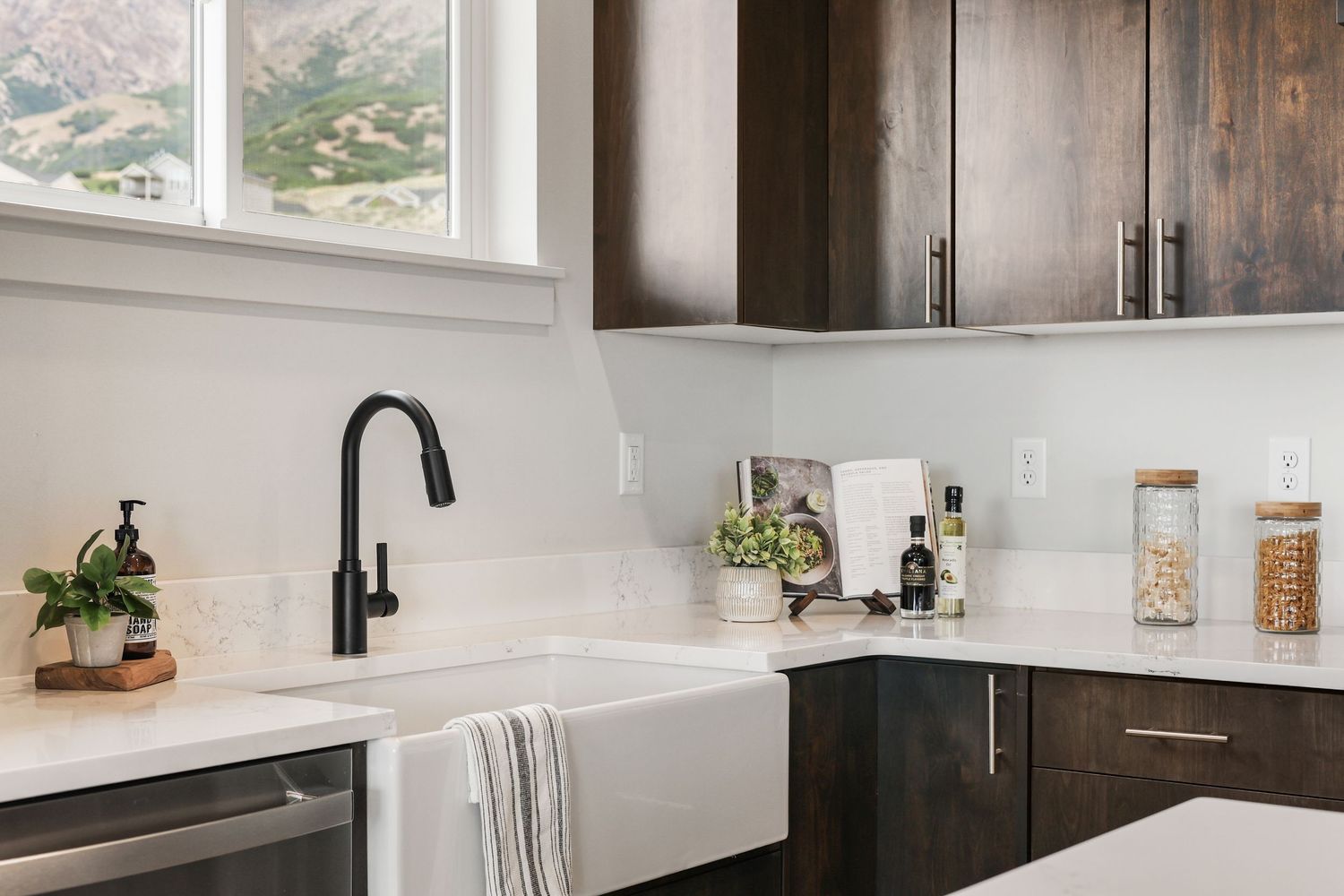 Modern kitchen with dark wood cabinets, white farmhouse sink, quartz countertops, and black faucet. Captured by Slate Media (best in UT)