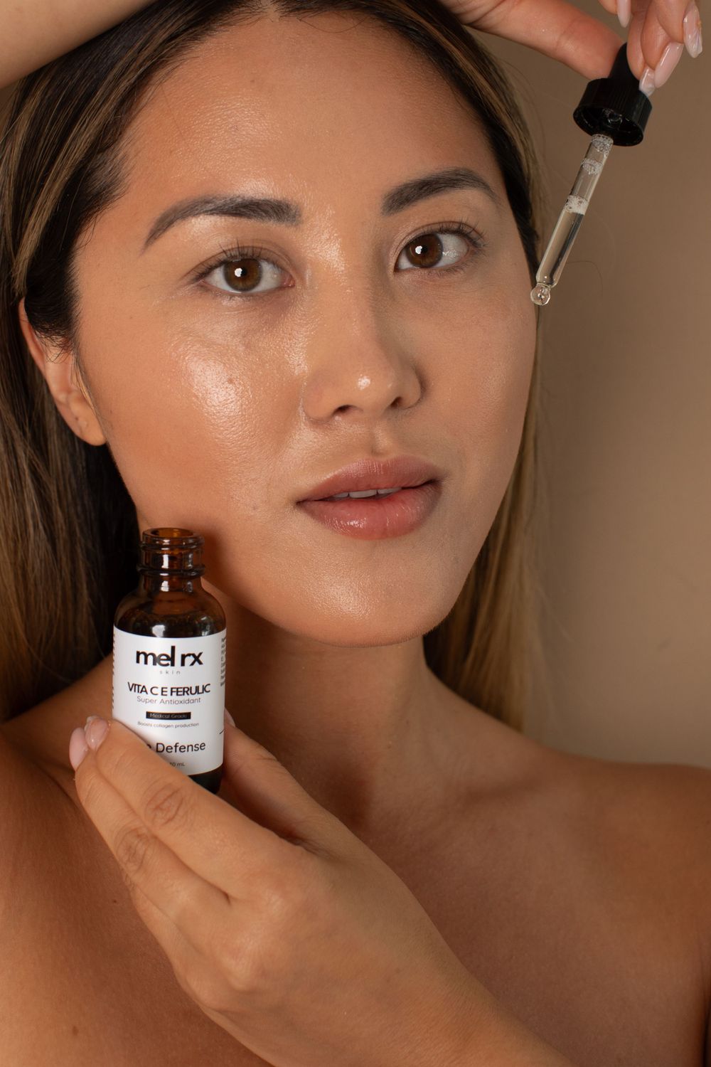 A person holds a dropper bottle of skincare serum against a neutral backdrop.