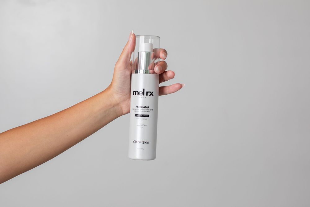 Hand holding white mel.rx cosmetic bottle against gray background.