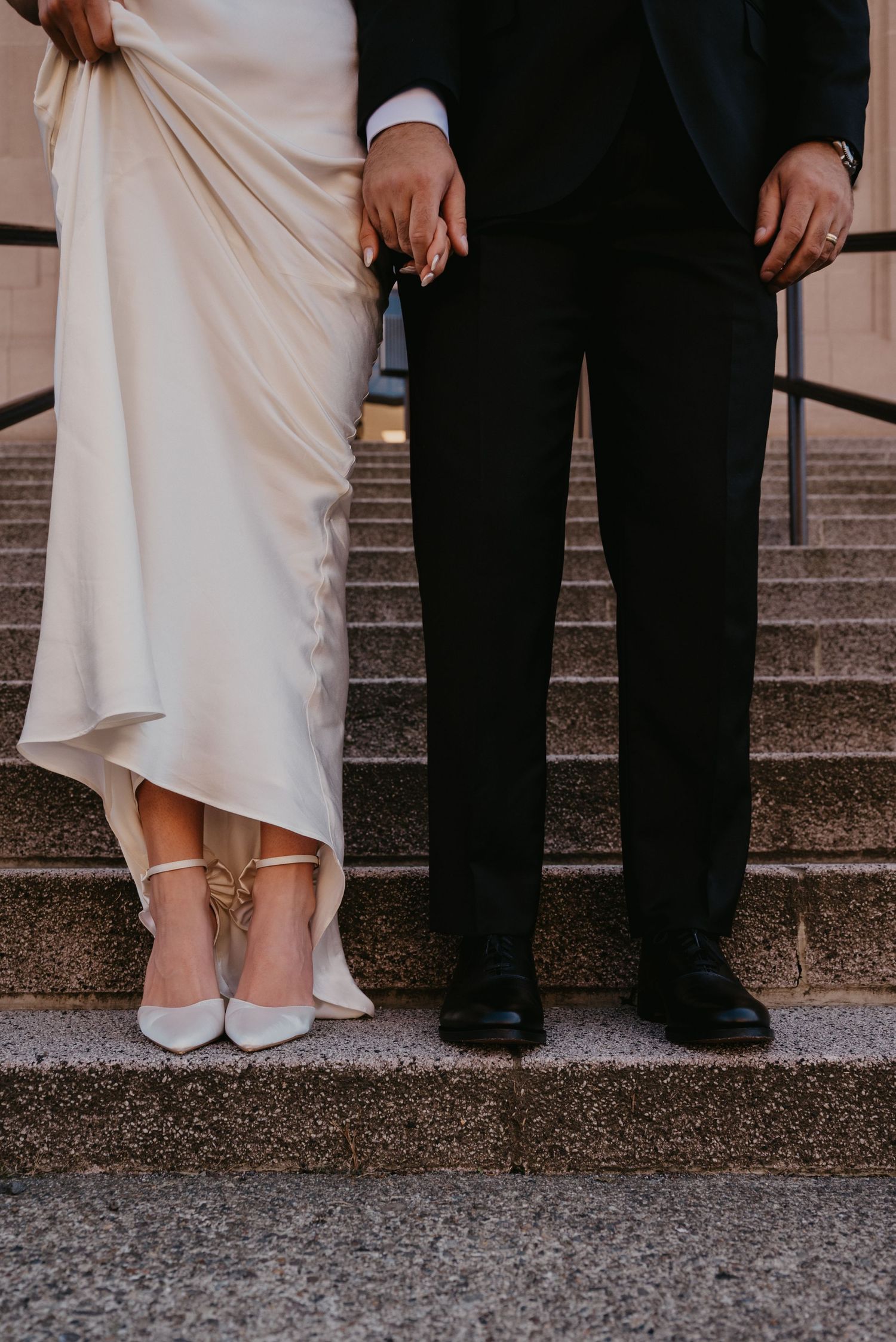 Close up of bride and groom's feet on stone steps, showing wedding dress and formal shoes.