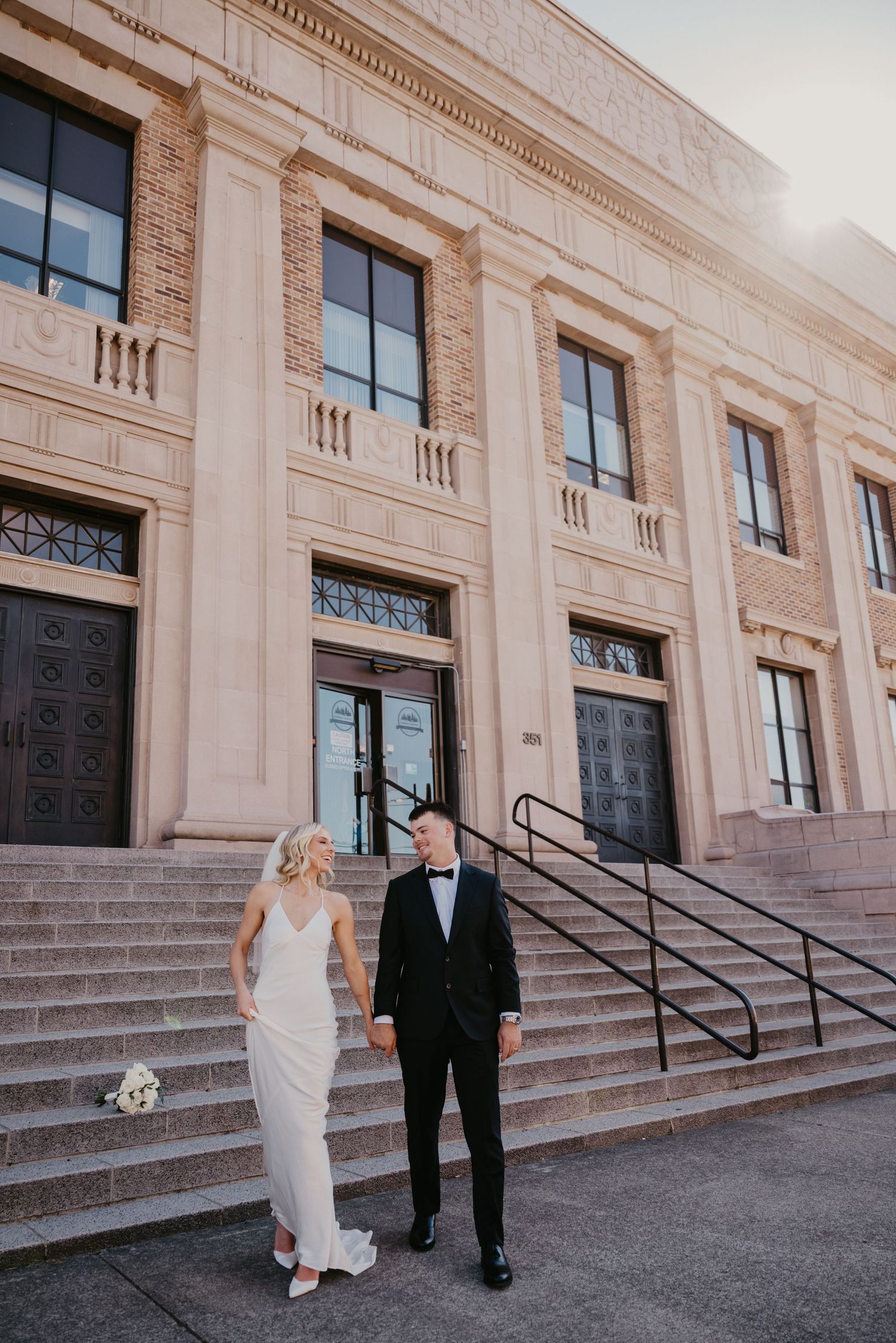 Newlyweds stand on stone steps in front of a historic building.