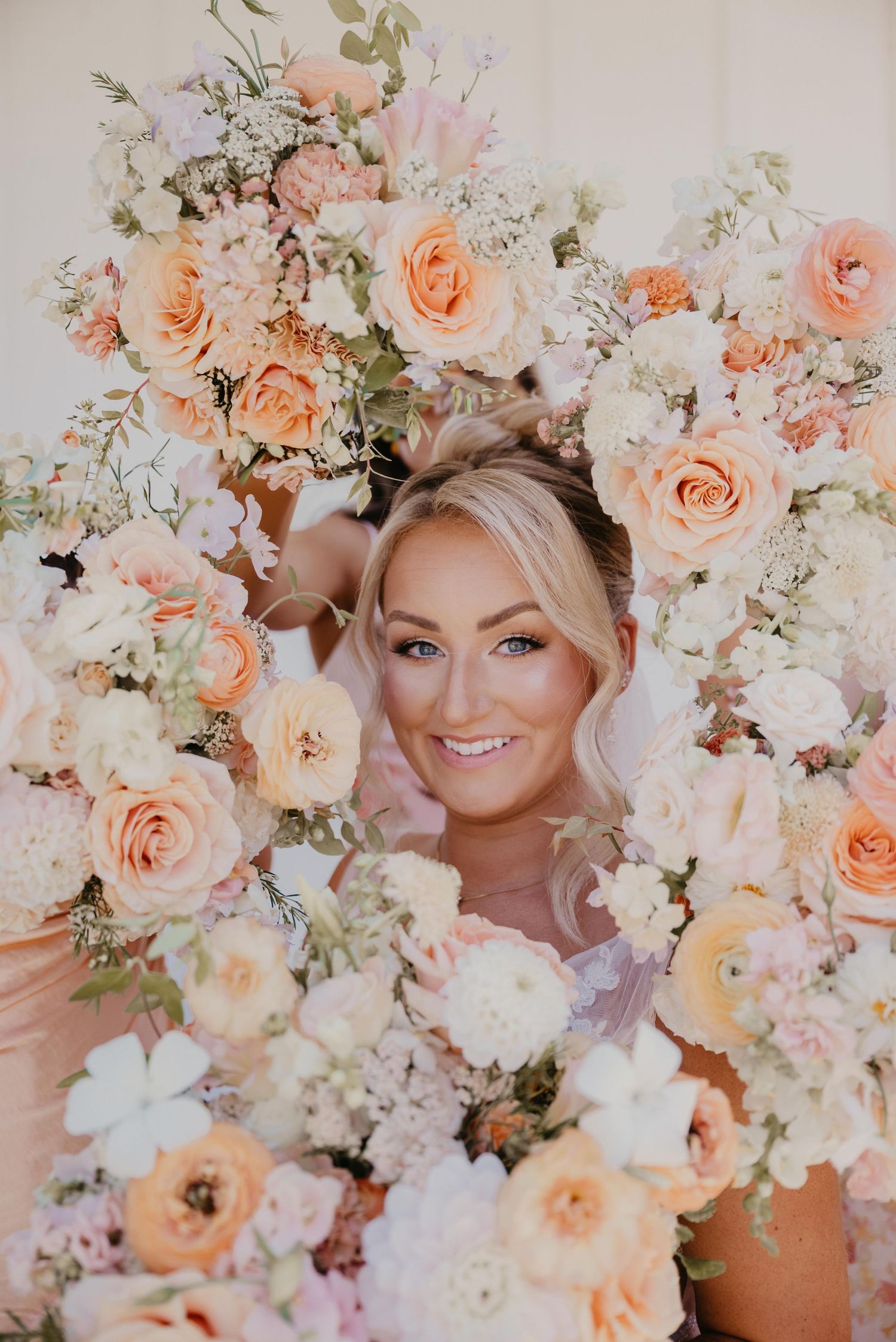 Dreamy floral portrait series surrounded by peach roses and white baby's breath in soft ethereal lighting.