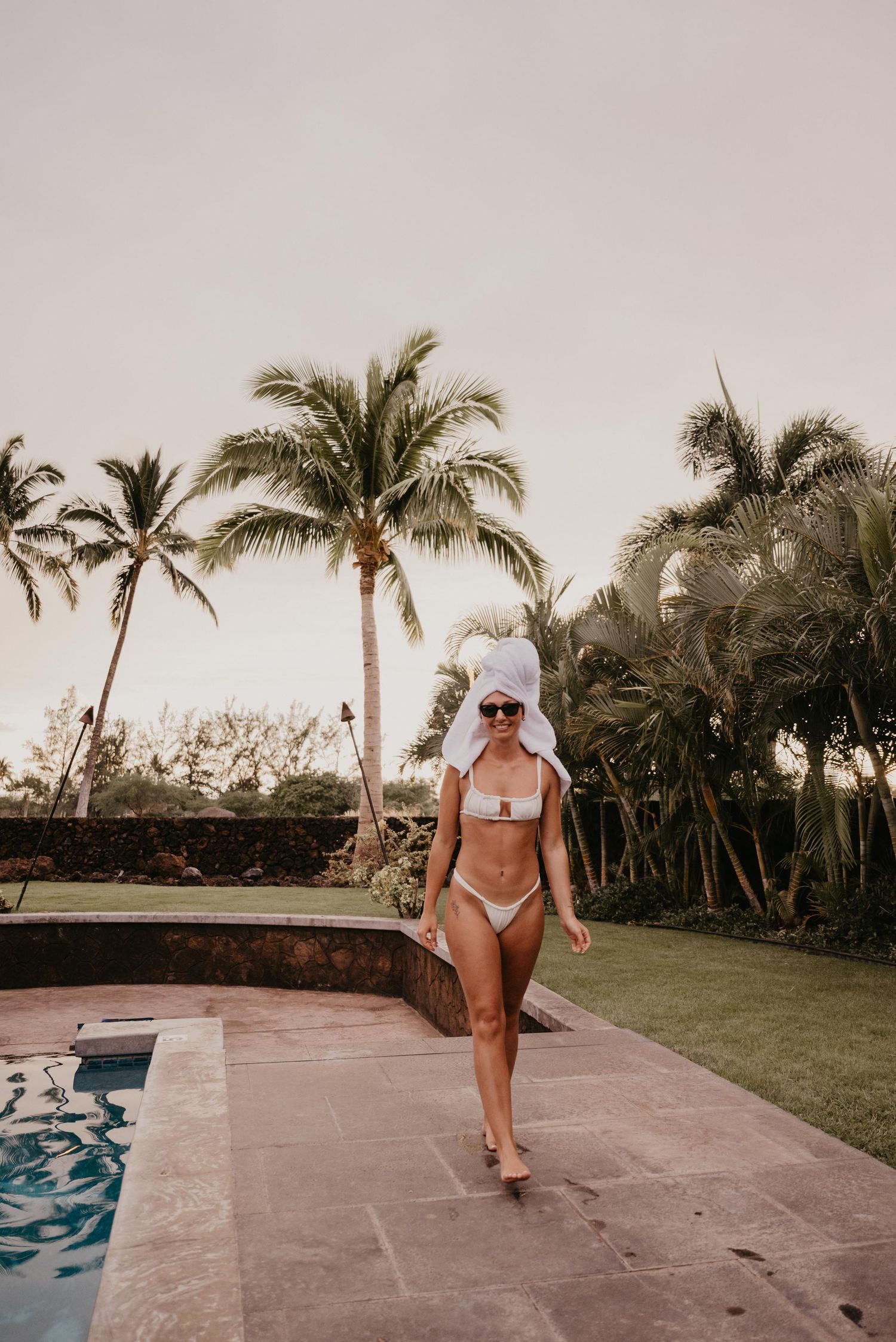 A three-panel sequence showing someone in a white bikini walking along a tiled patio with palm trees in the background.