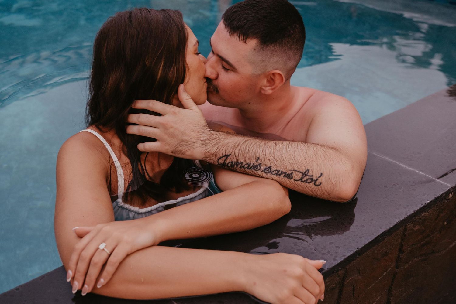A romantic couple share an intimate moment together in a pool at dusk.
