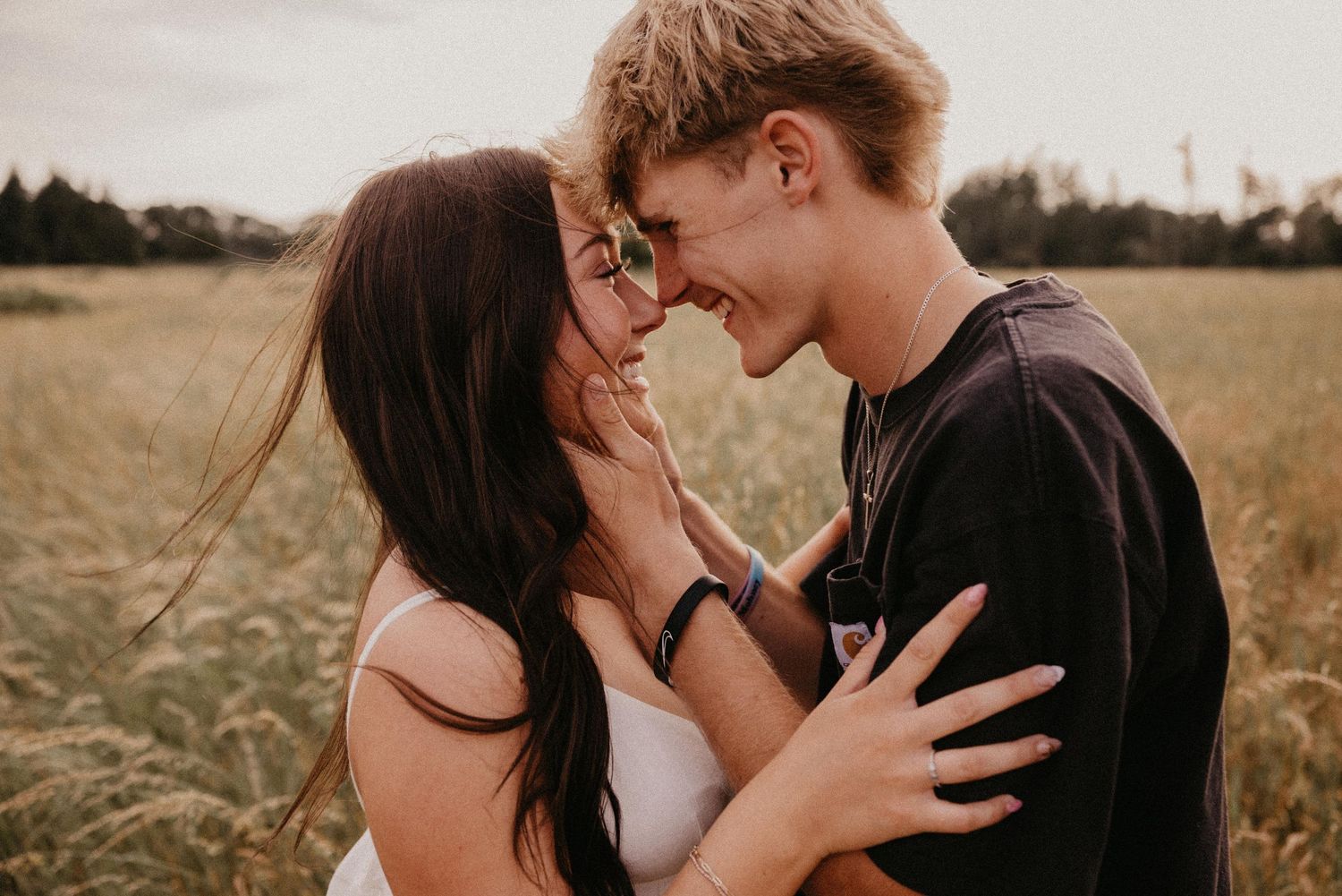 Young couple embraces tenderly in a golden field during sunset, sharing intimate romantic moments.