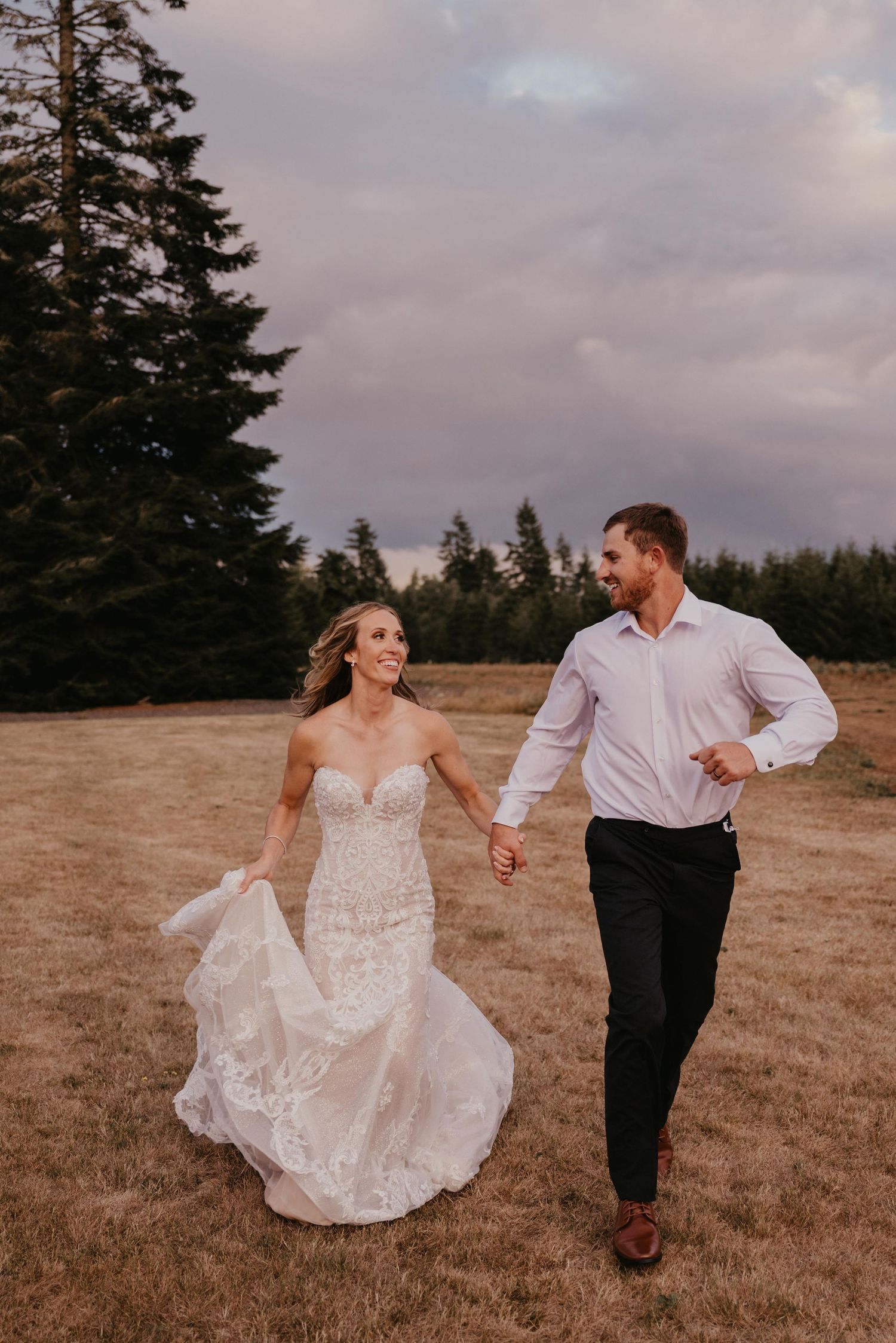 A couple runs through a field holding hands at sunset during their wedding photo session.
