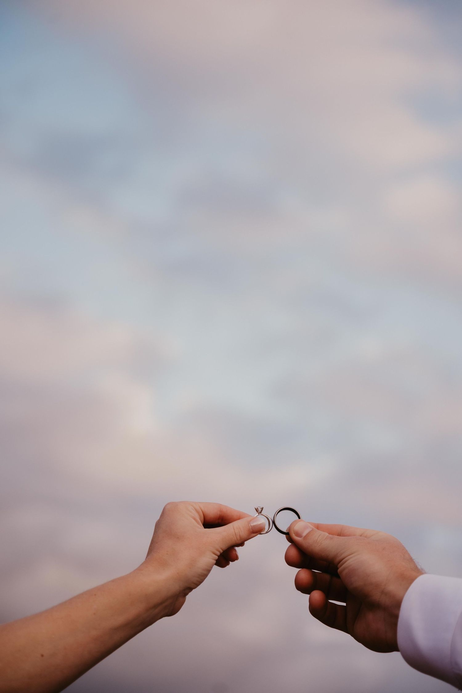 Two hands reaching towards each other against a cloudy sky background, capturing an intimate moment of connection.