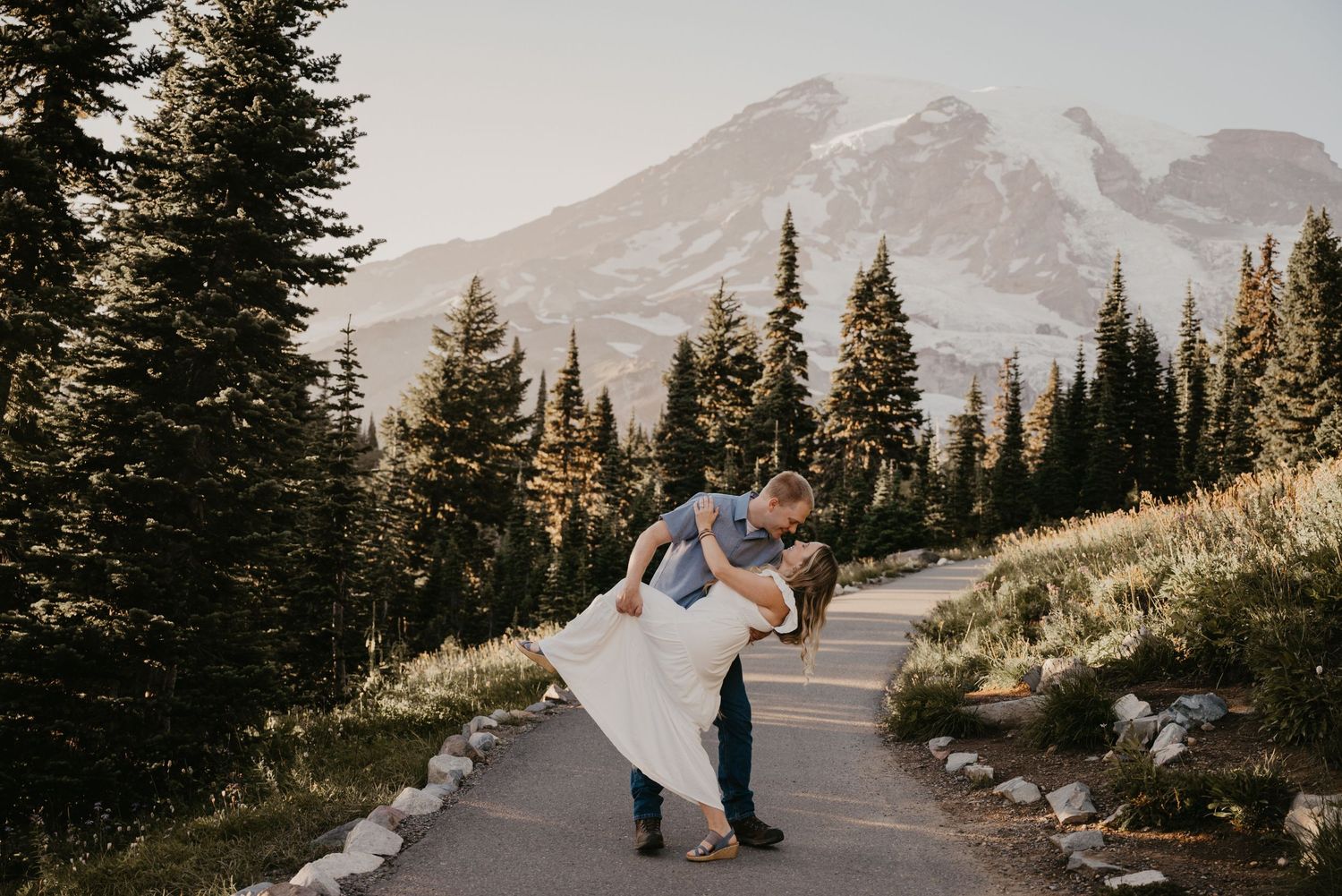 Couple embraces on a mountain path with snow-capped peaks in the background.