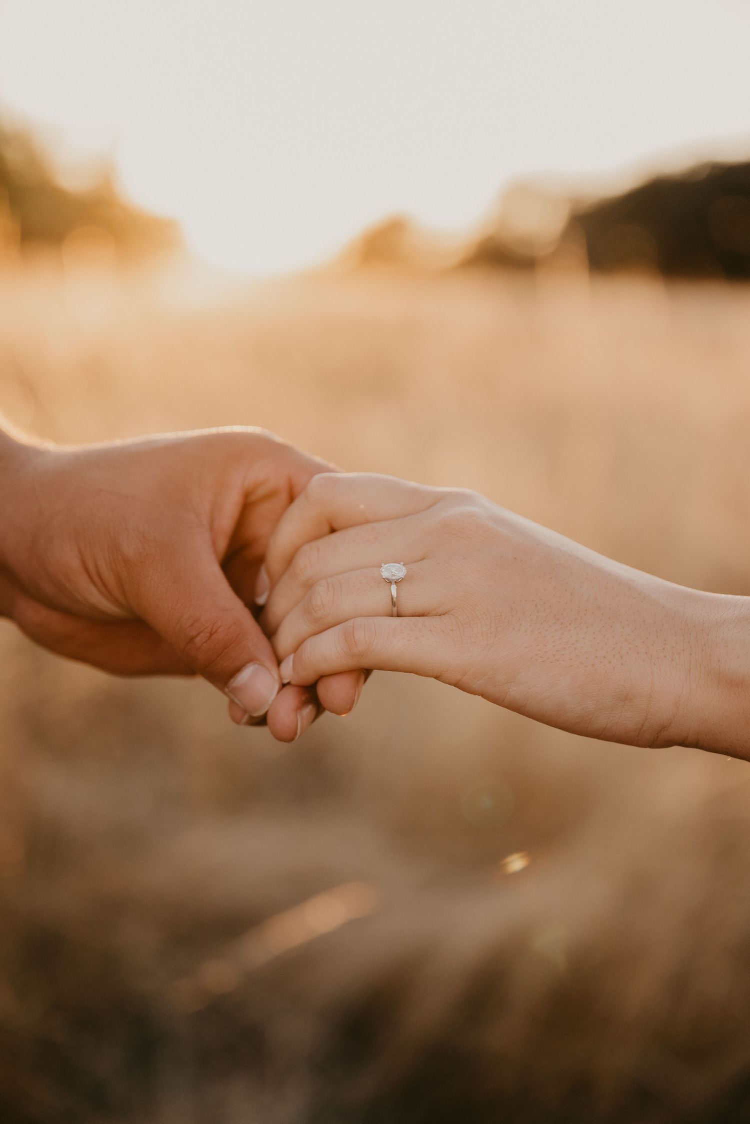 Close-up of hands holding with engagement ring during golden hour sunset.