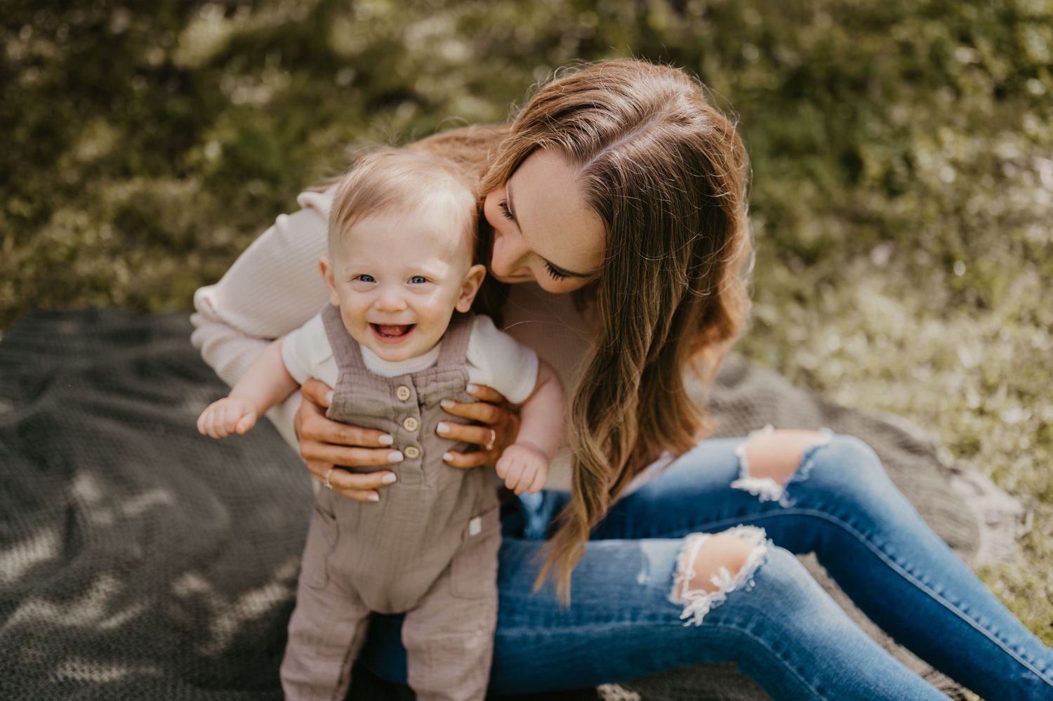 Mother and baby share joyful moment together outdoors on a blanket.
