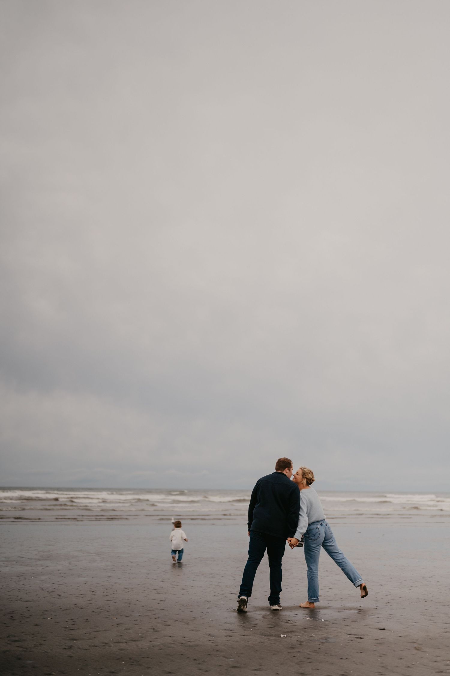 A couple and small child share an intimate moment on a misty beach shoreline.