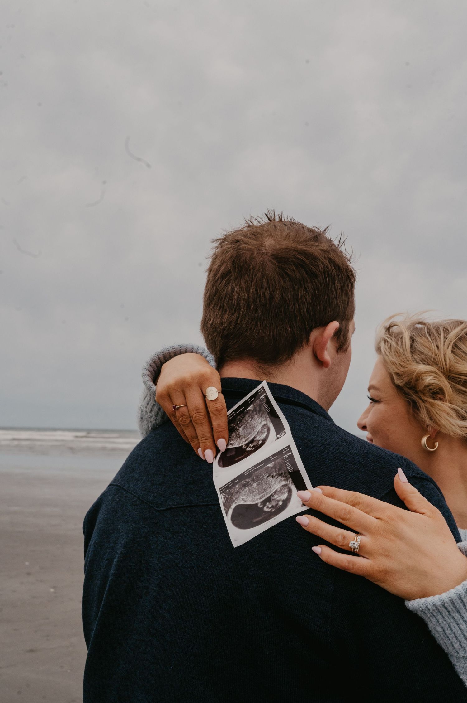 A couple on a beach sharing an ultrasound photo together.