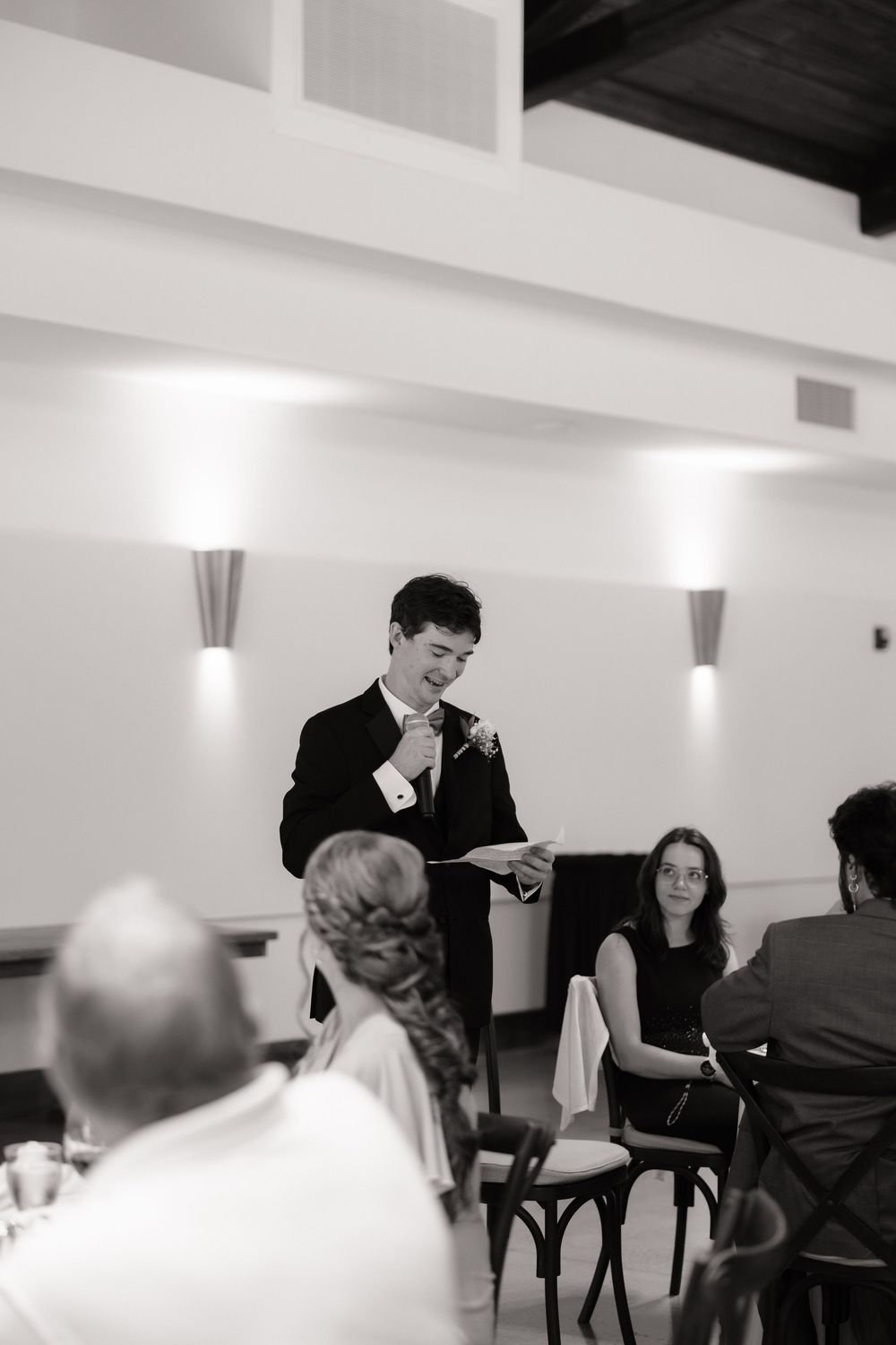 Black and white photo of groomsman delivering heartfelt wedding speech at elegant reception.
