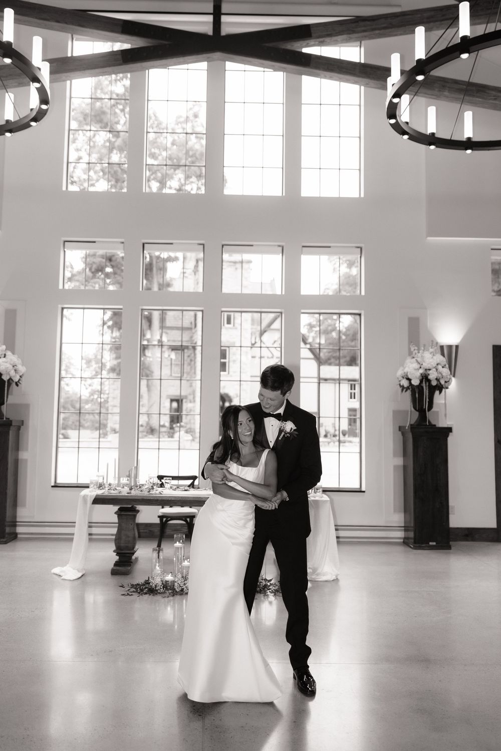 Bride and groom share romantic first dance in bright elegant wedding venue with tall windows.