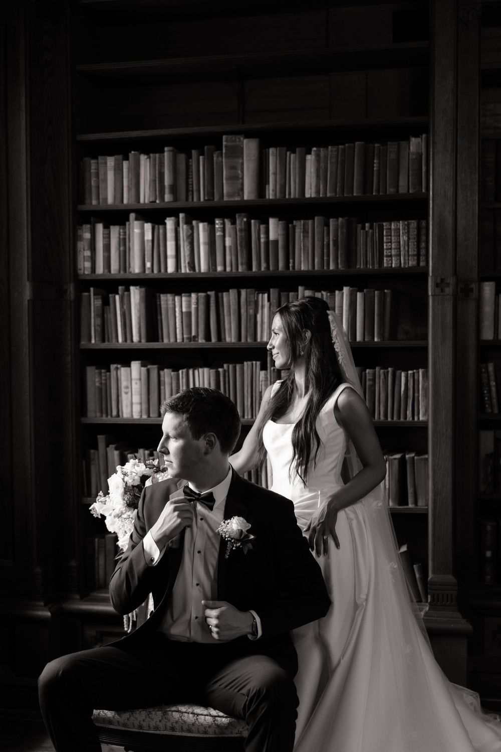 Elegant black and white wedding photo of bride and groom posing in a classic library setting.