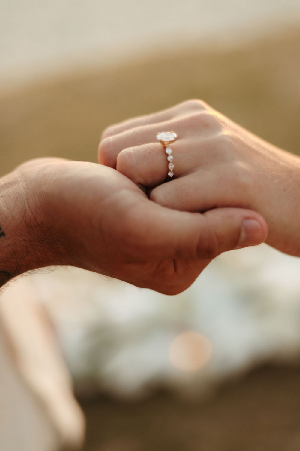 Two hands holding together, woman wearing elegant oval diamond engagement ring with pavé band on ring finger.