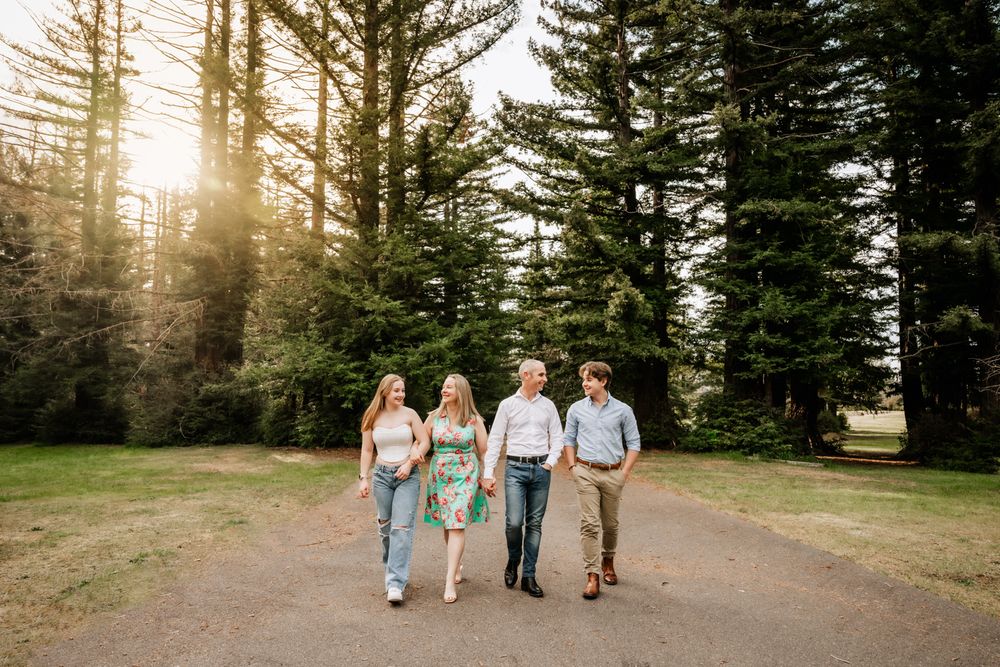 Group walking together on a tree-lined path with sunlight streaming through tall evergreens.