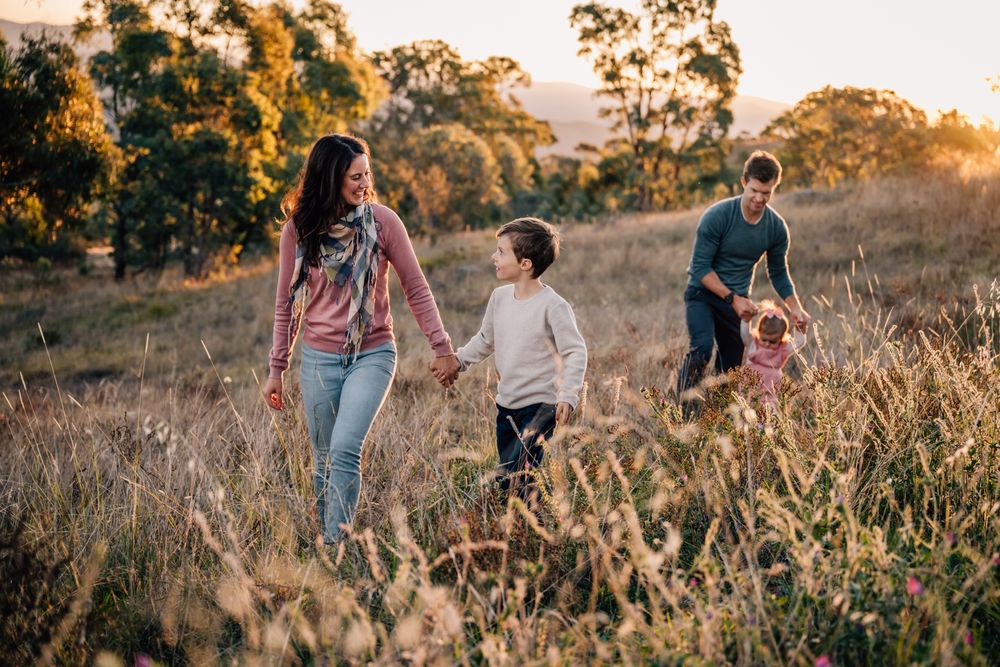 Family walking together through tall grass field during golden hour.