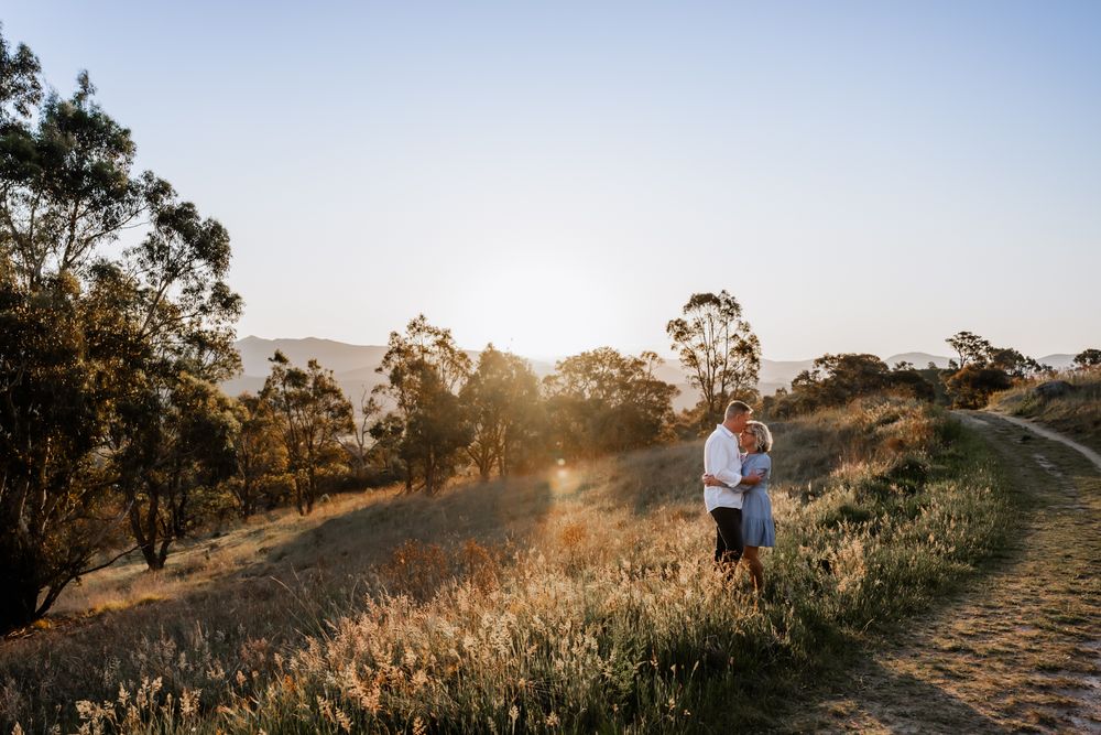 Two people standing on a scenic hilltop trail during golden hour with trees in the background.