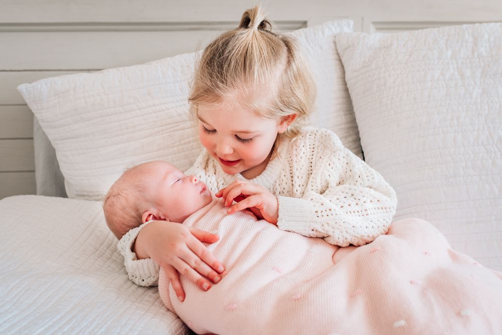 Two young children sharing a tender moment on a white bed with soft natural lighting.