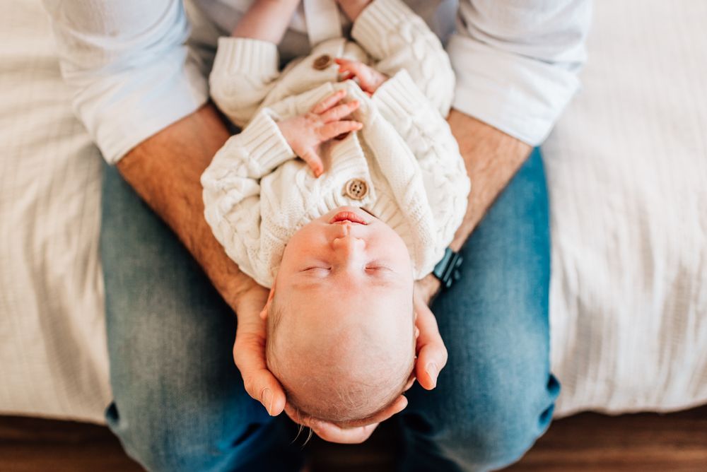 Overhead view of an infant resting peacefully on someone's lap in soft white clothing.
