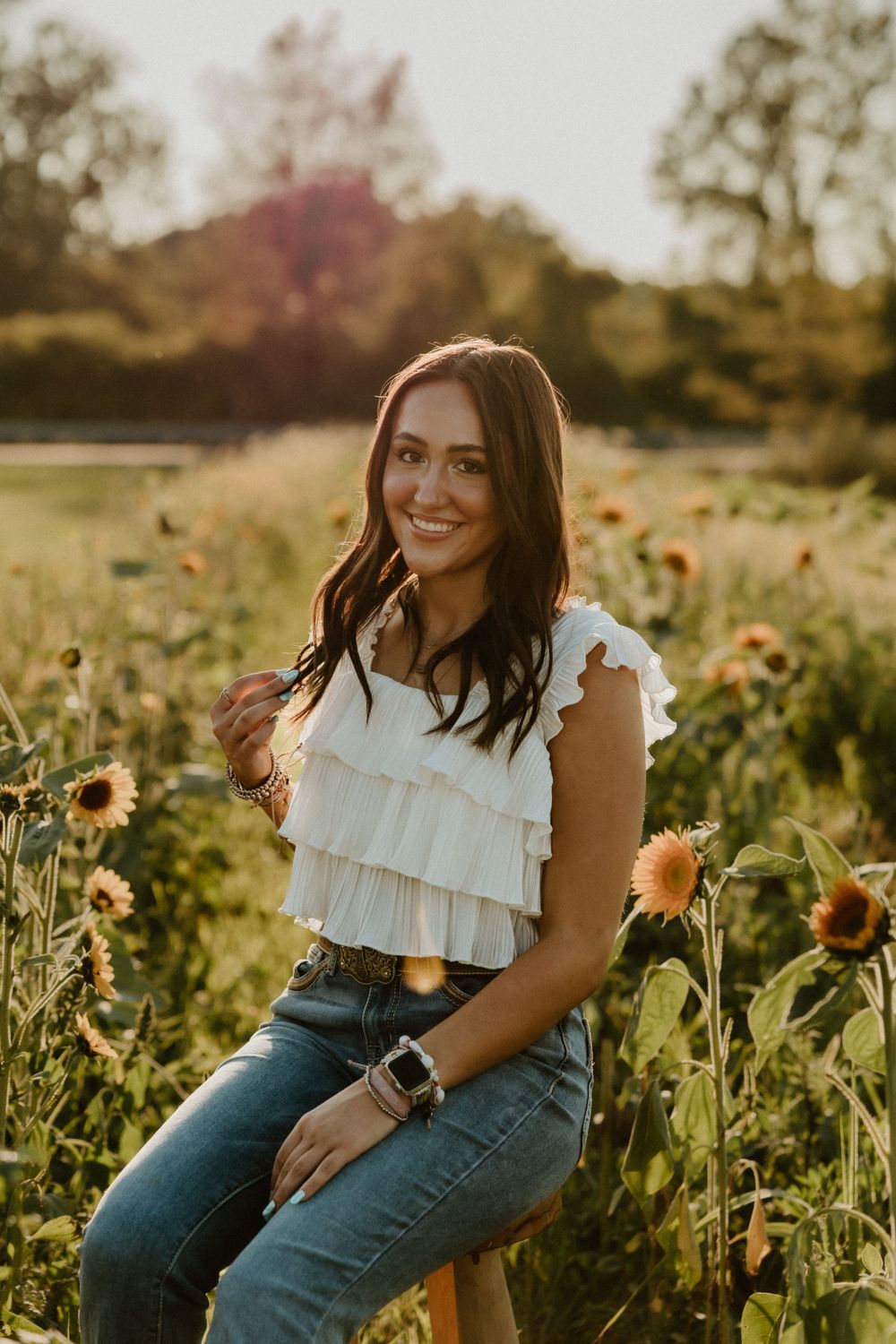 Portrait in a ruffled white top and jeans amid blooming sunflowers at sunset.