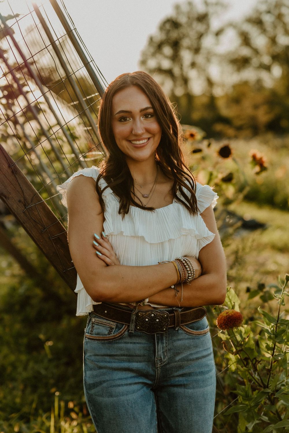 Casual outdoor portrait with ruffled white top and jeans against wooden structure and sunflowers.