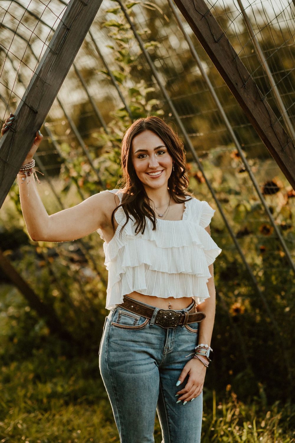 Outdoor portrait by wooden structure wearing white ruffled top and denim in golden sunlight.