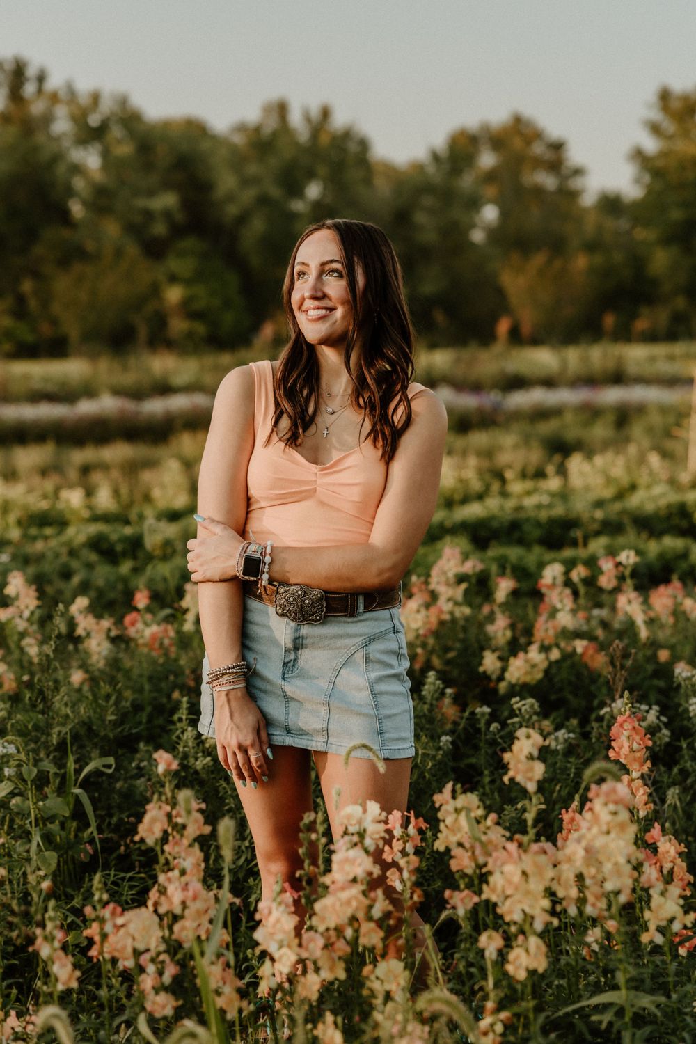 Outdoor portrait in peach top and denim shorts surrounded by wildflowers at sunset.