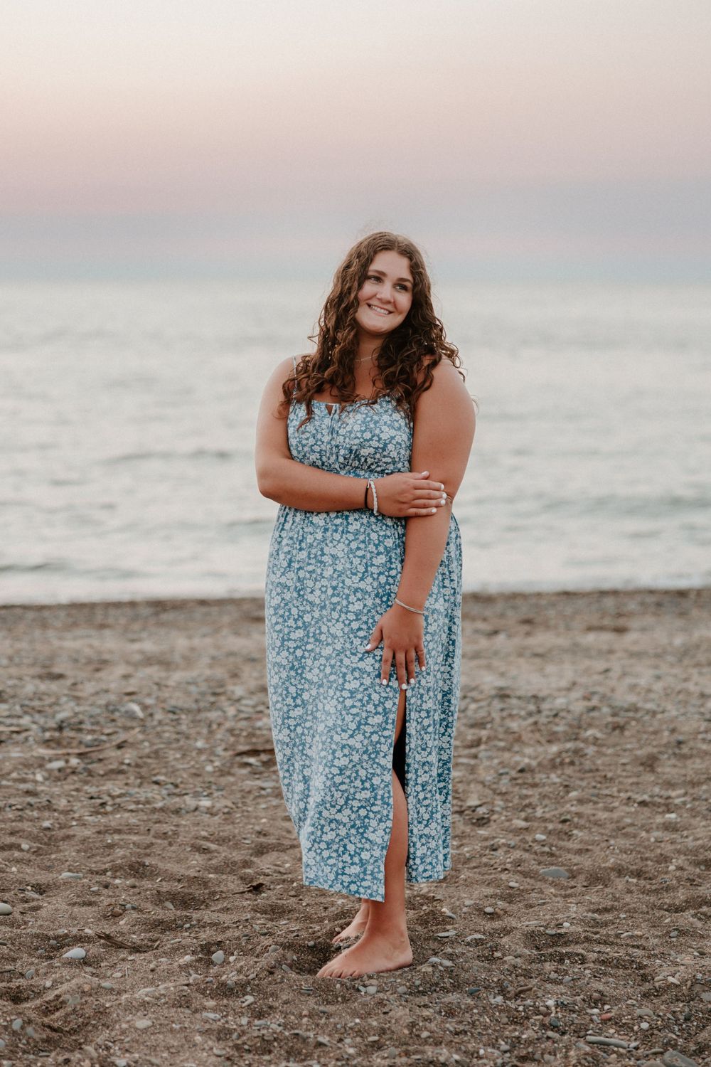 A person wearing a blue floral maxi dress poses on a beach at dusk.