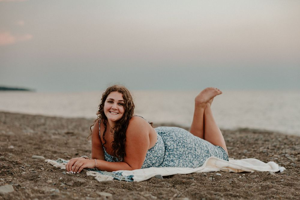 A person in a floral sundress lying on a beach blanket during sunset.