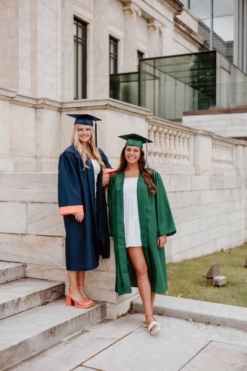 Graduates in navy and green robes pose on stone steps of university building.