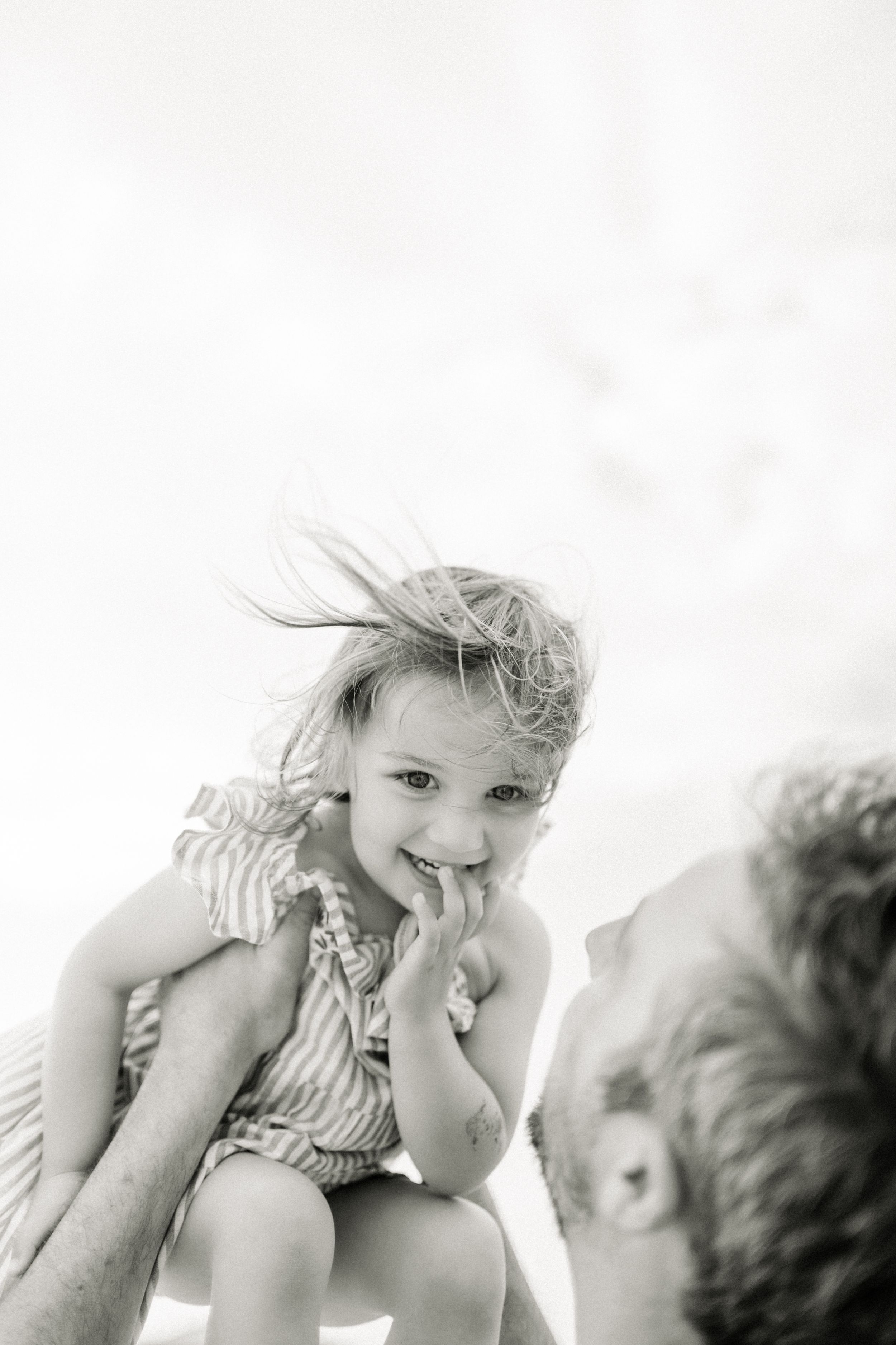 Black and white photo capturing a joyful moment between parent and child against a bright sky backdrop.