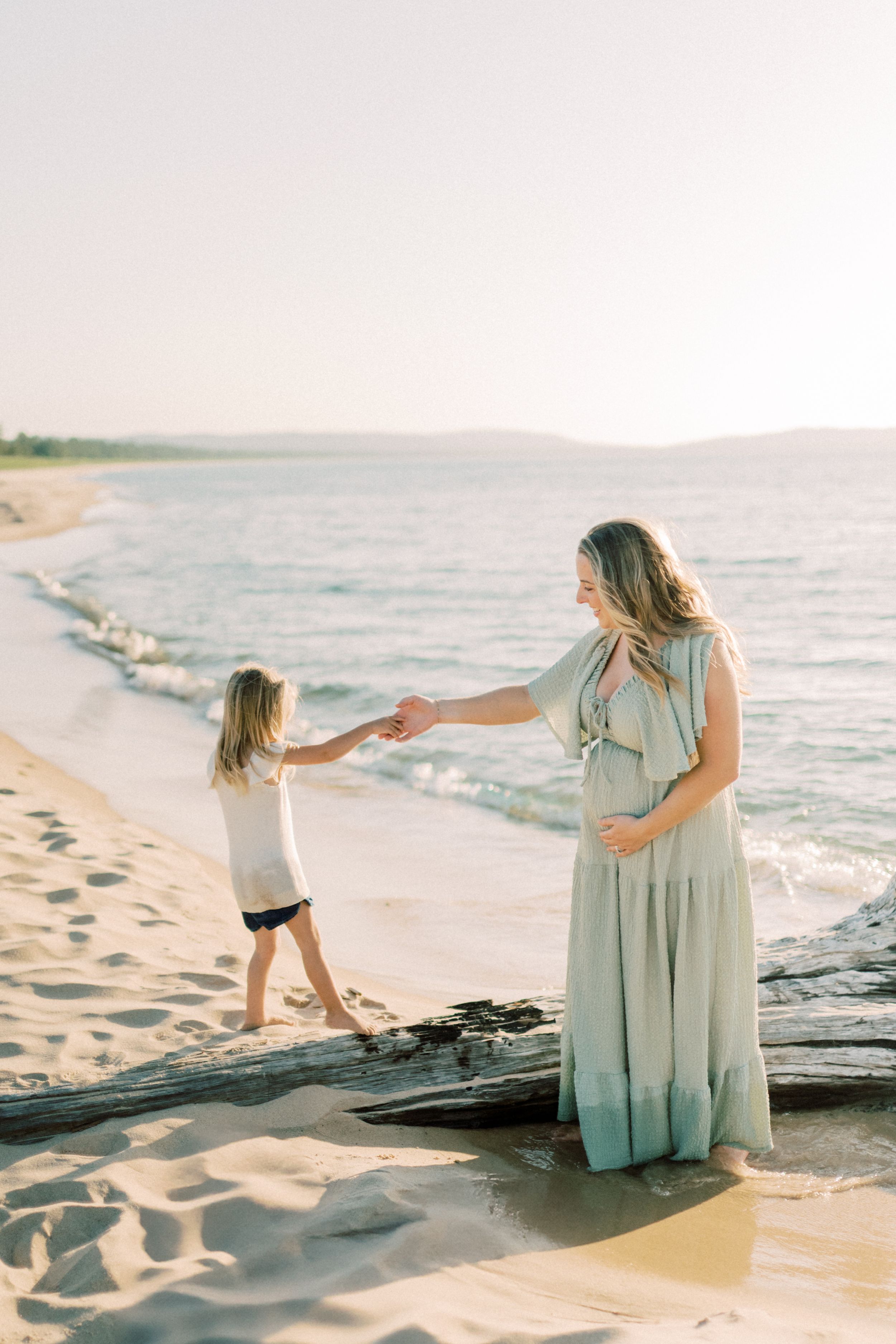 A tender beach scene at sunset with two people holding hands along the surf's edge in matching mint-colored outfits.