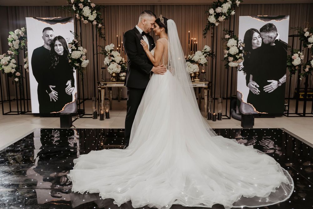 Wedding couple embraces on a black reflective floor with portrait displays in the background.