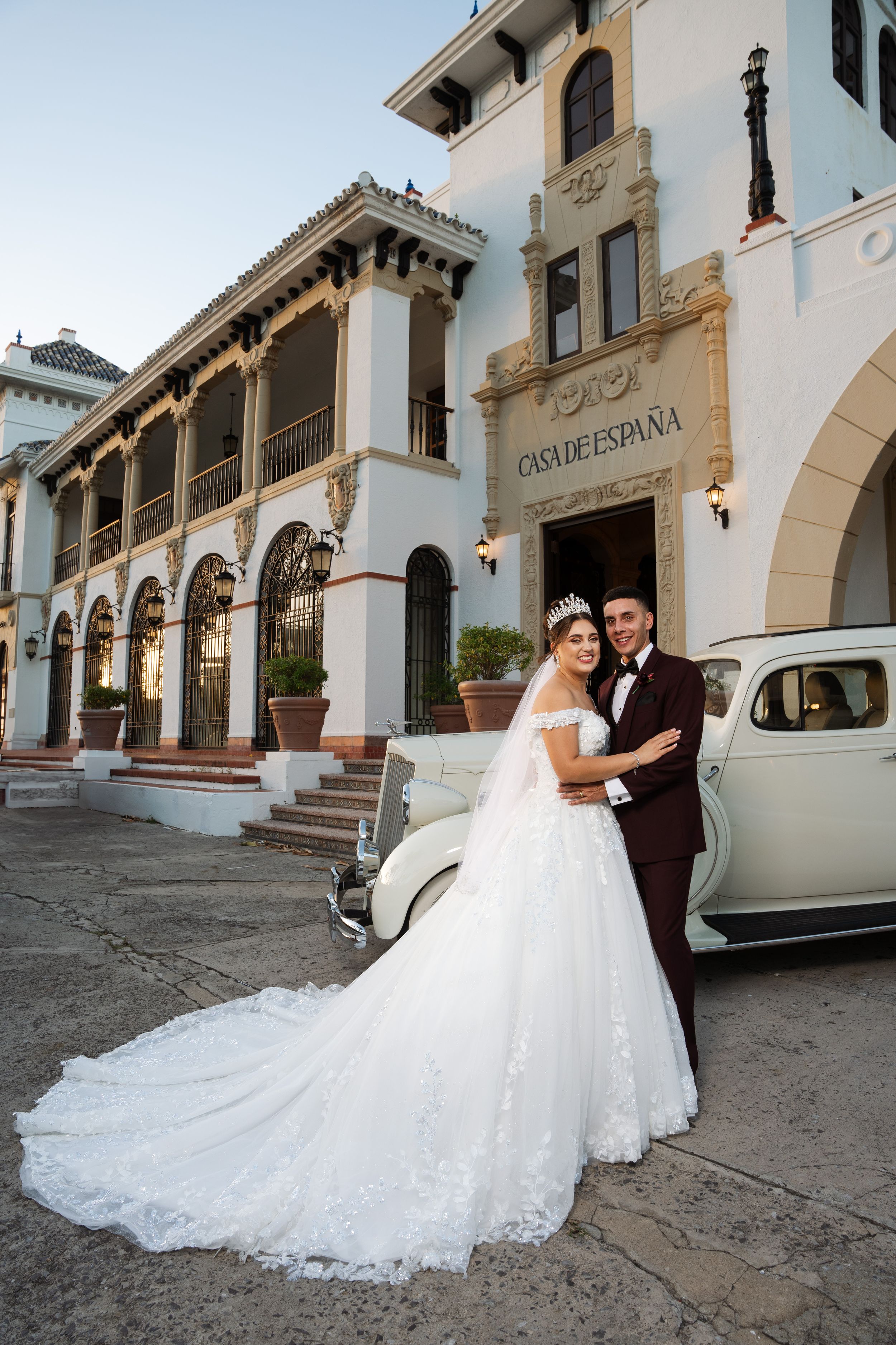 A classic wedding photo in front of Casa de España with a vintage car and Spanish colonial architecture.