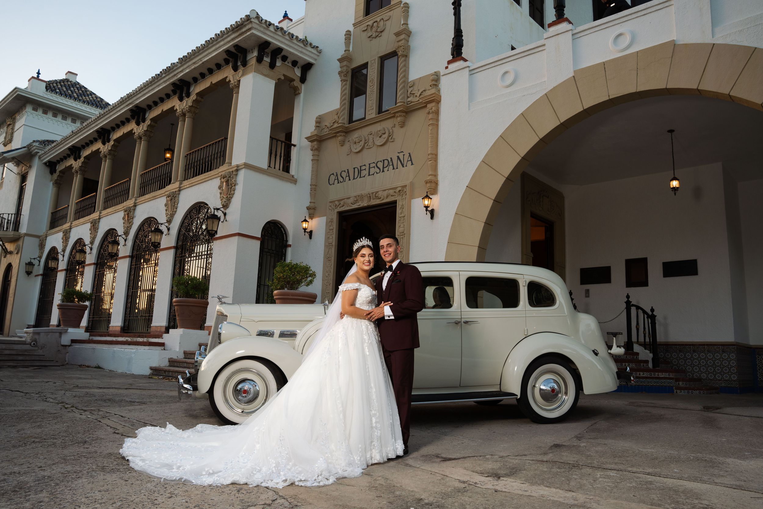 Elegant wedding portrait with vintage car at Casa de España featuring Spanish colonial architecture.