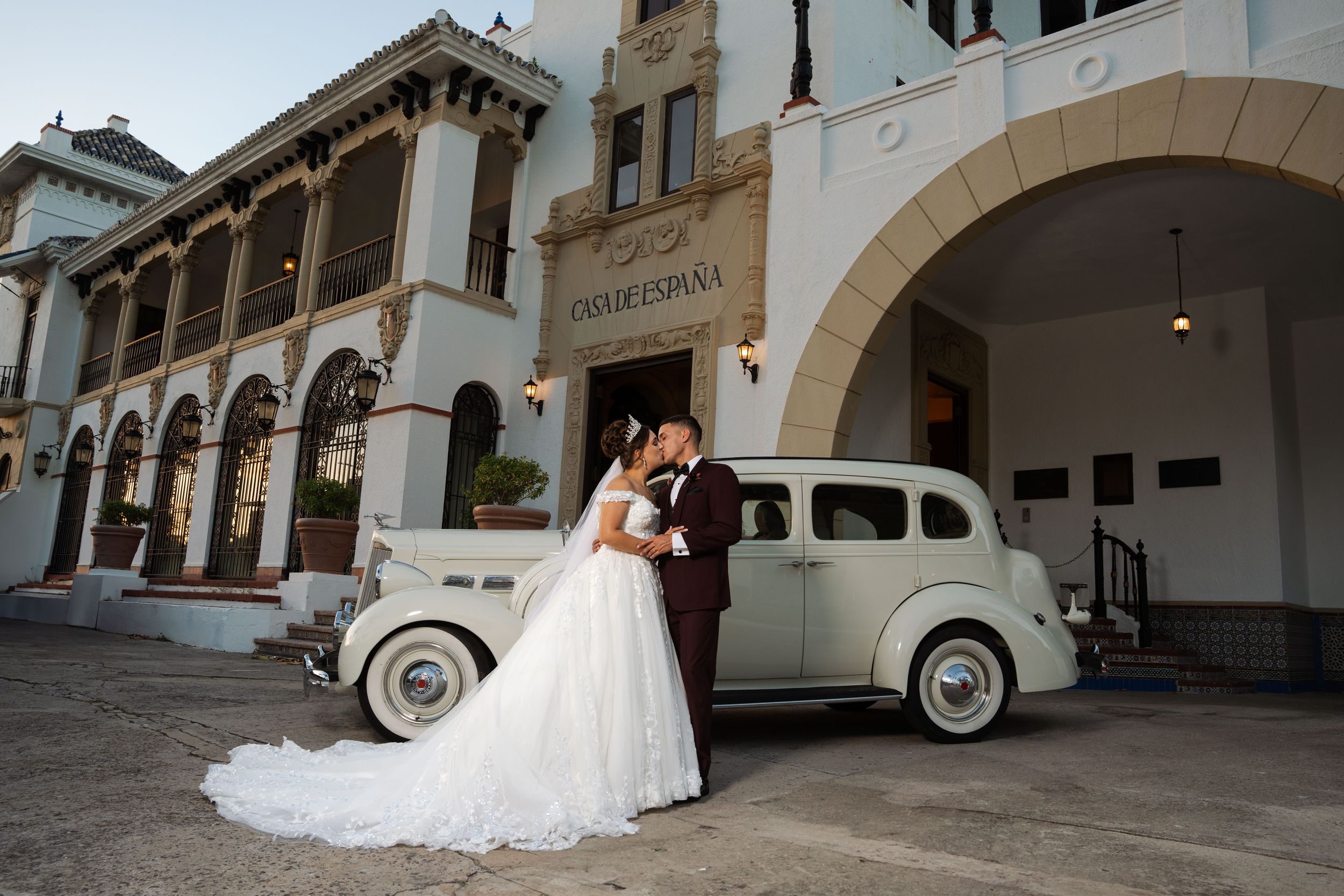 Elegant wedding photo with a vintage car and Spanish colonial architecture in the background.