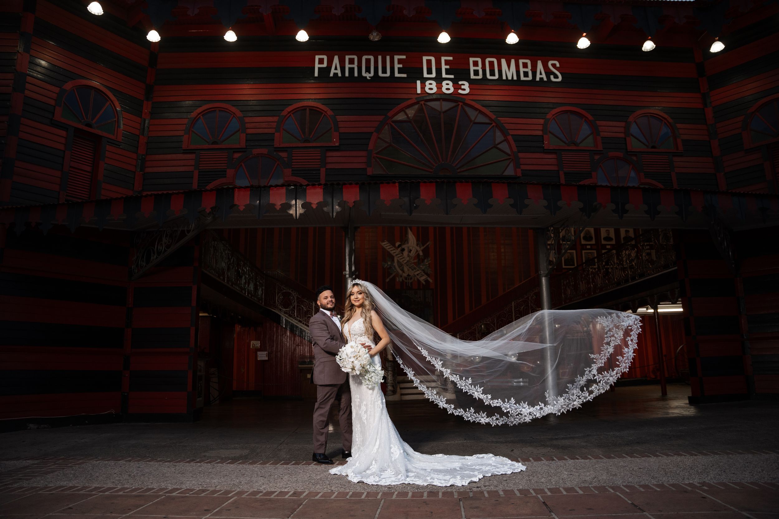 Dramatic wedding photo with flowing veil in a dark theater with 'PARQUE DE BOMBAS' signage.