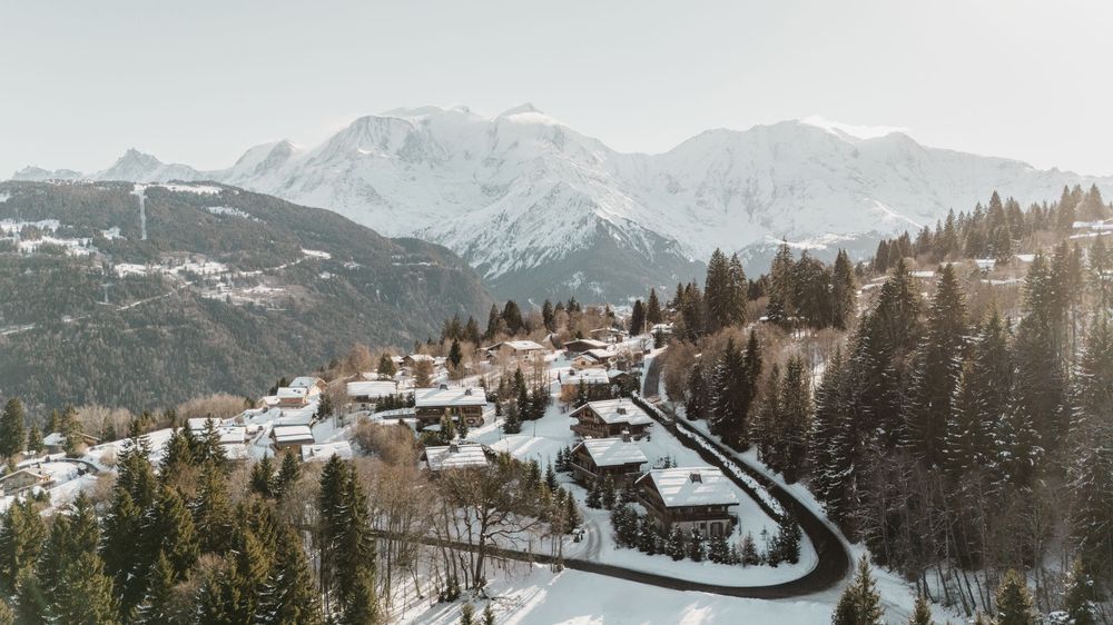 Aerial winter drone view of snow-covered alpine village with pine forest and mountain peaks — French Alps drone photography — Paul Brechu