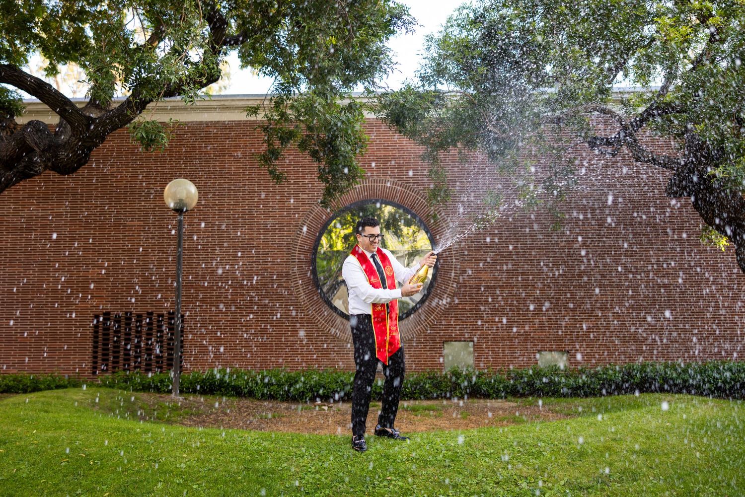 A celebratory moment captured with confetti falling in a courtyard with brick walls and trees.