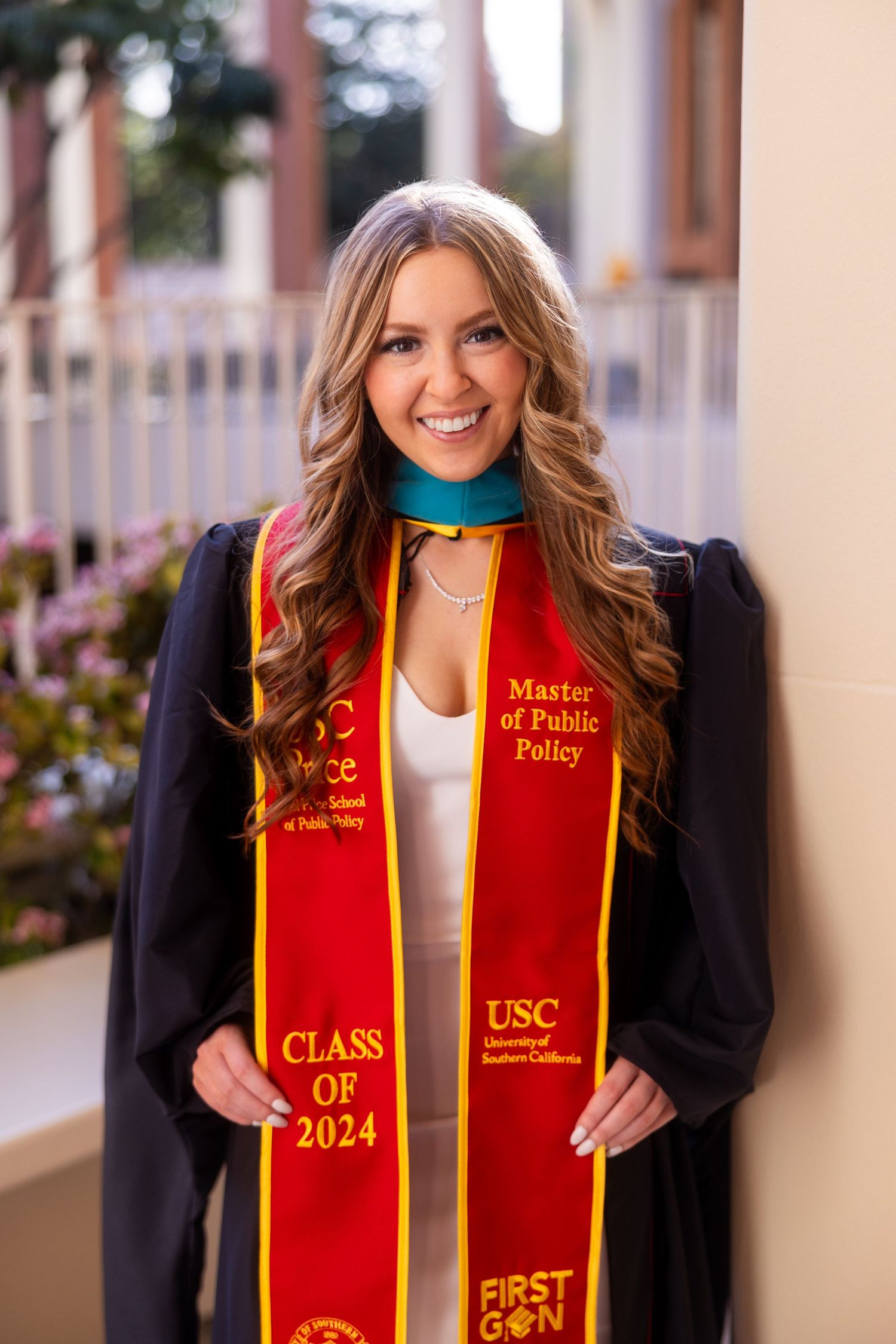 USC graduate wearing red and gold graduation stole and black gown smiles at camera.