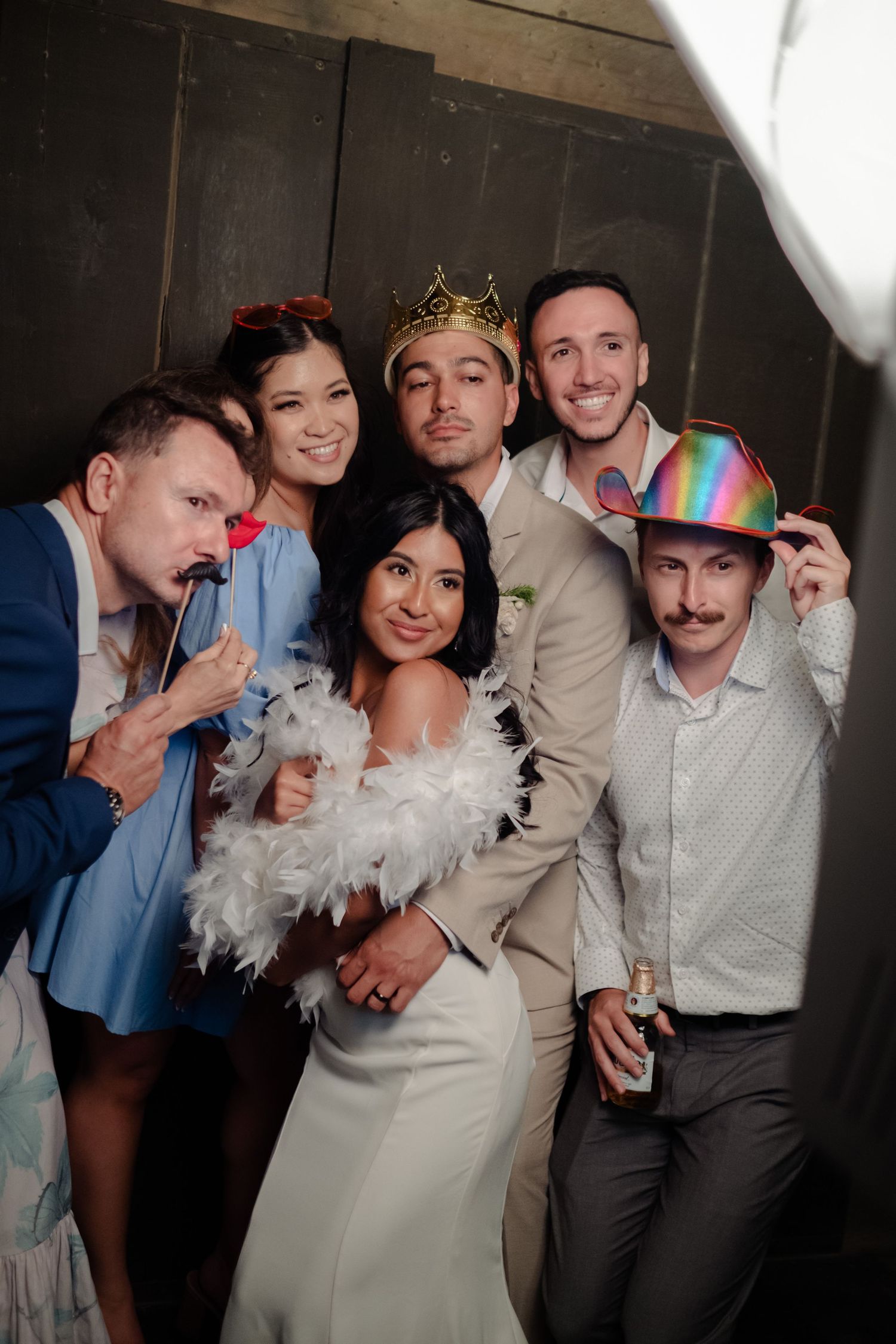 Wedding party group poses with fun photo booth props including crowns, hats, and mustaches.