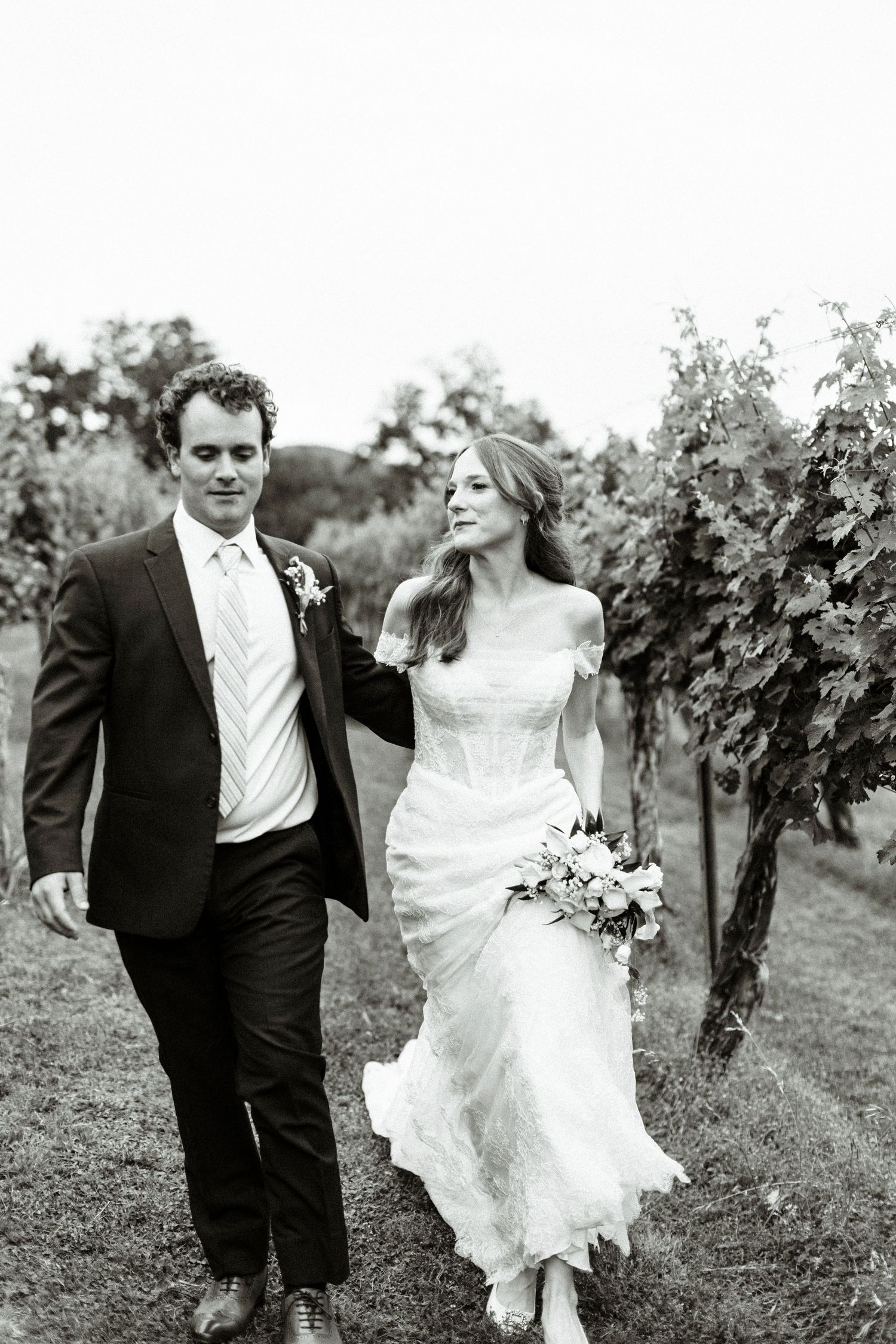 Black and white photo of bride and groom walking through vineyard in elegant wedding attire at wolf mountain vineyards in dahlonega georgia.