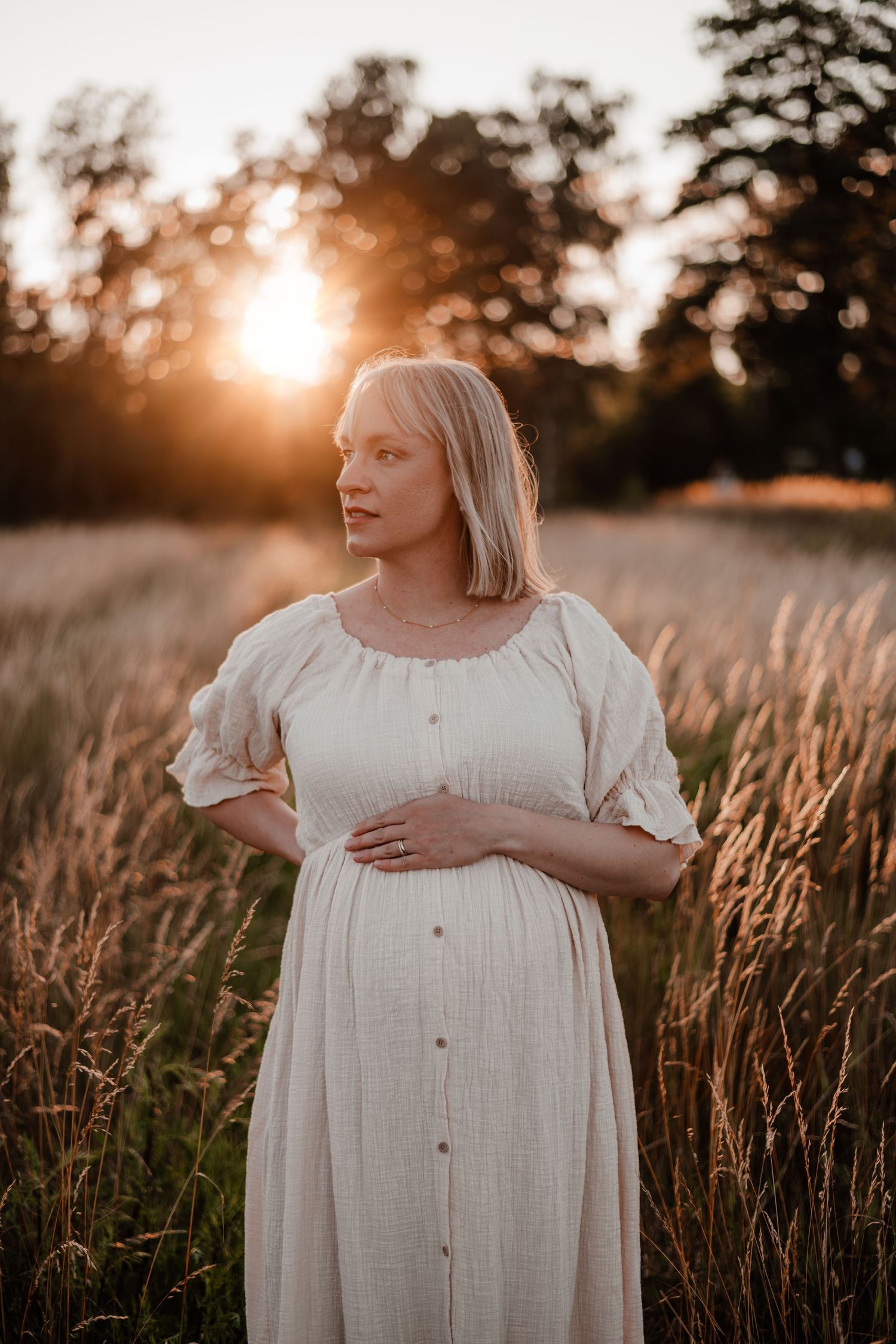 En gravid i en bohemisk klänning på en äng i solnedgången