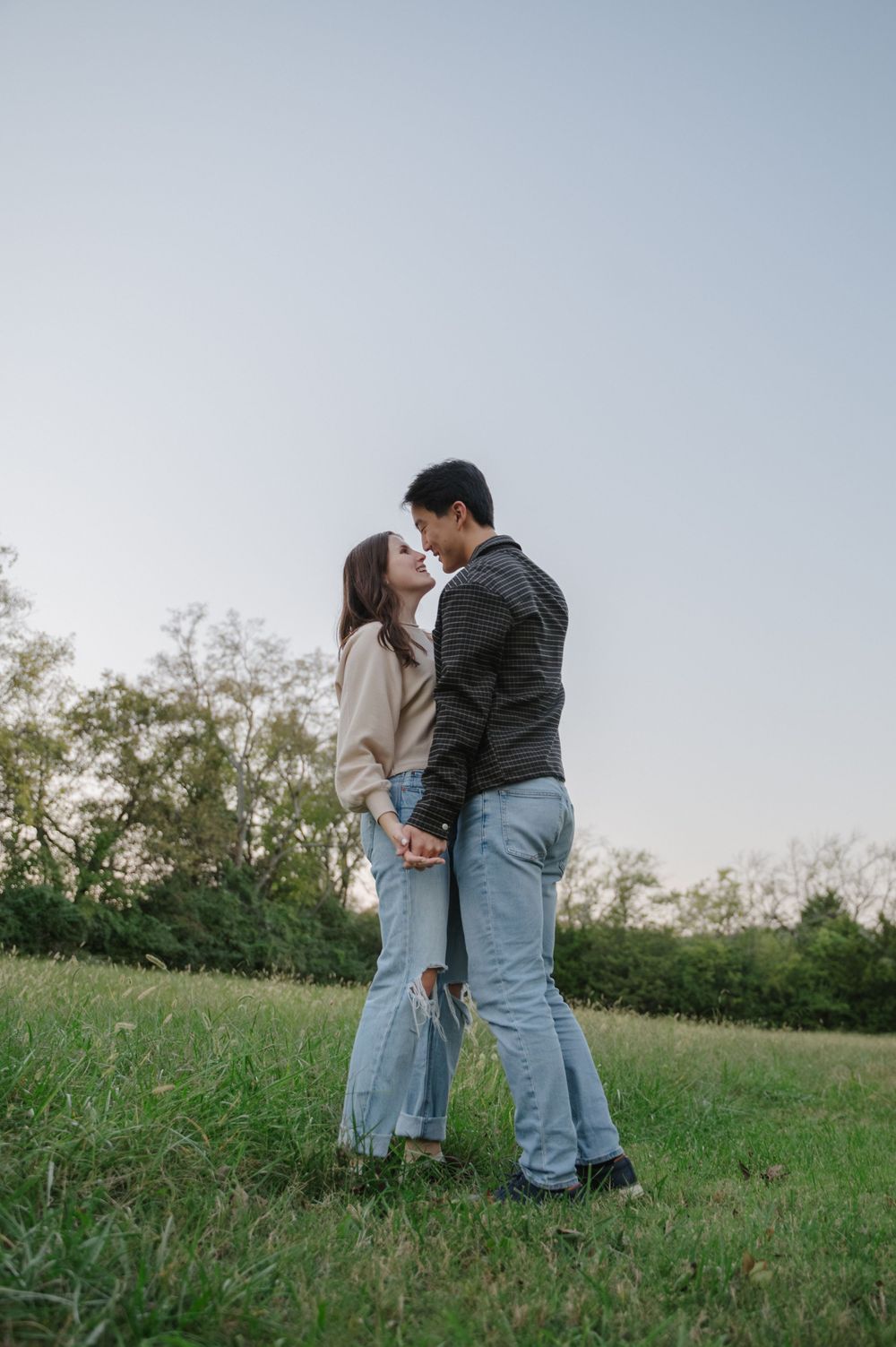 Engaged couple lean in for a kiss in a bright green, open field