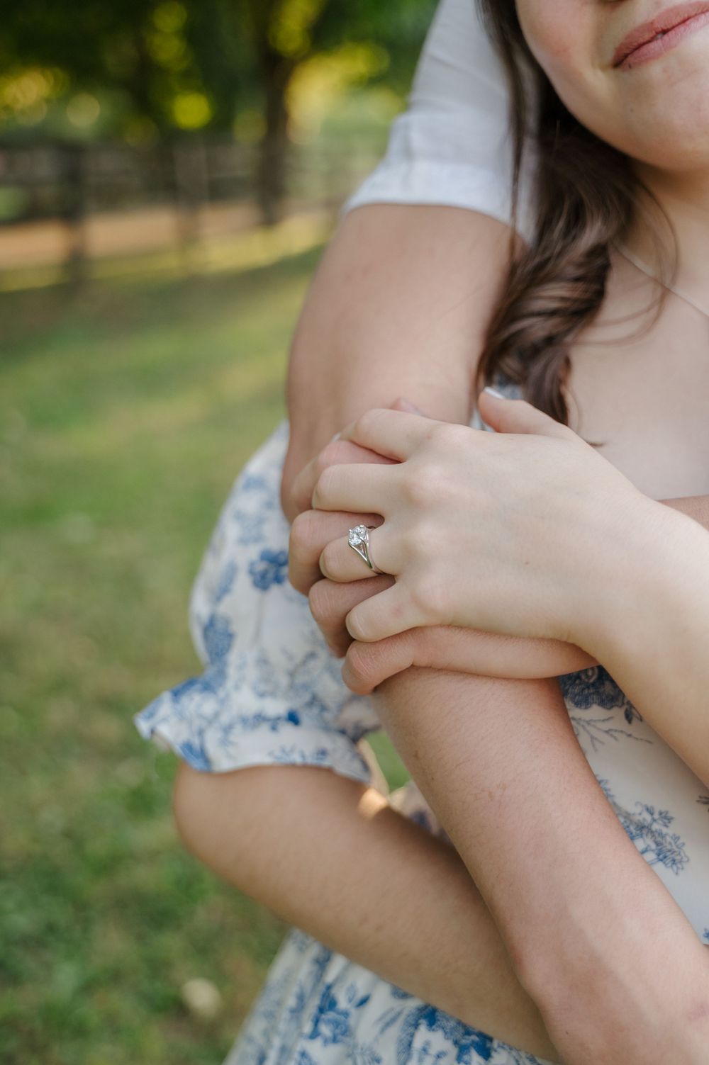 An engagement ring seen as couple hugs