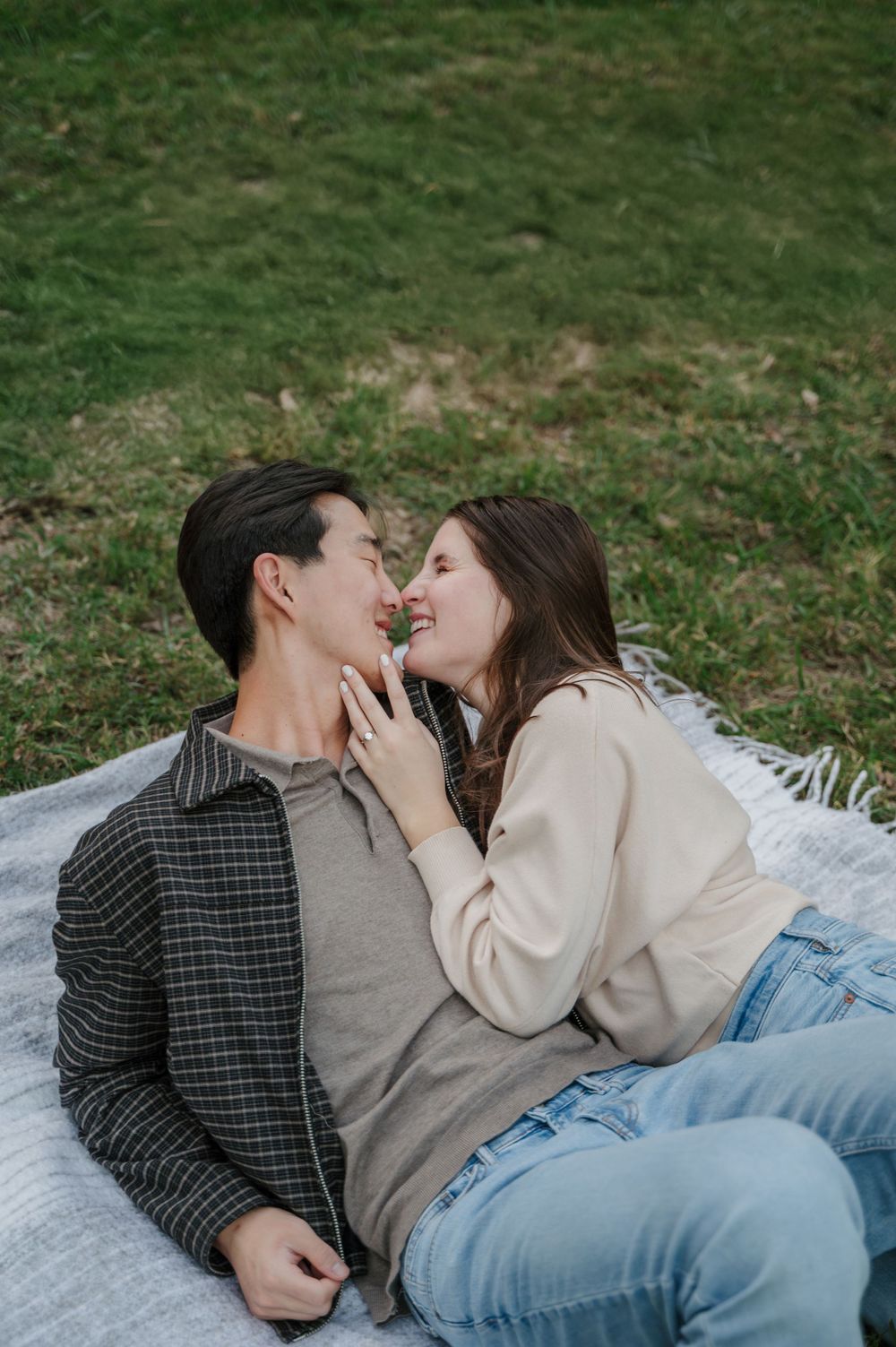 Girl leans to kiss fiancé as they lay together on picnic blanket